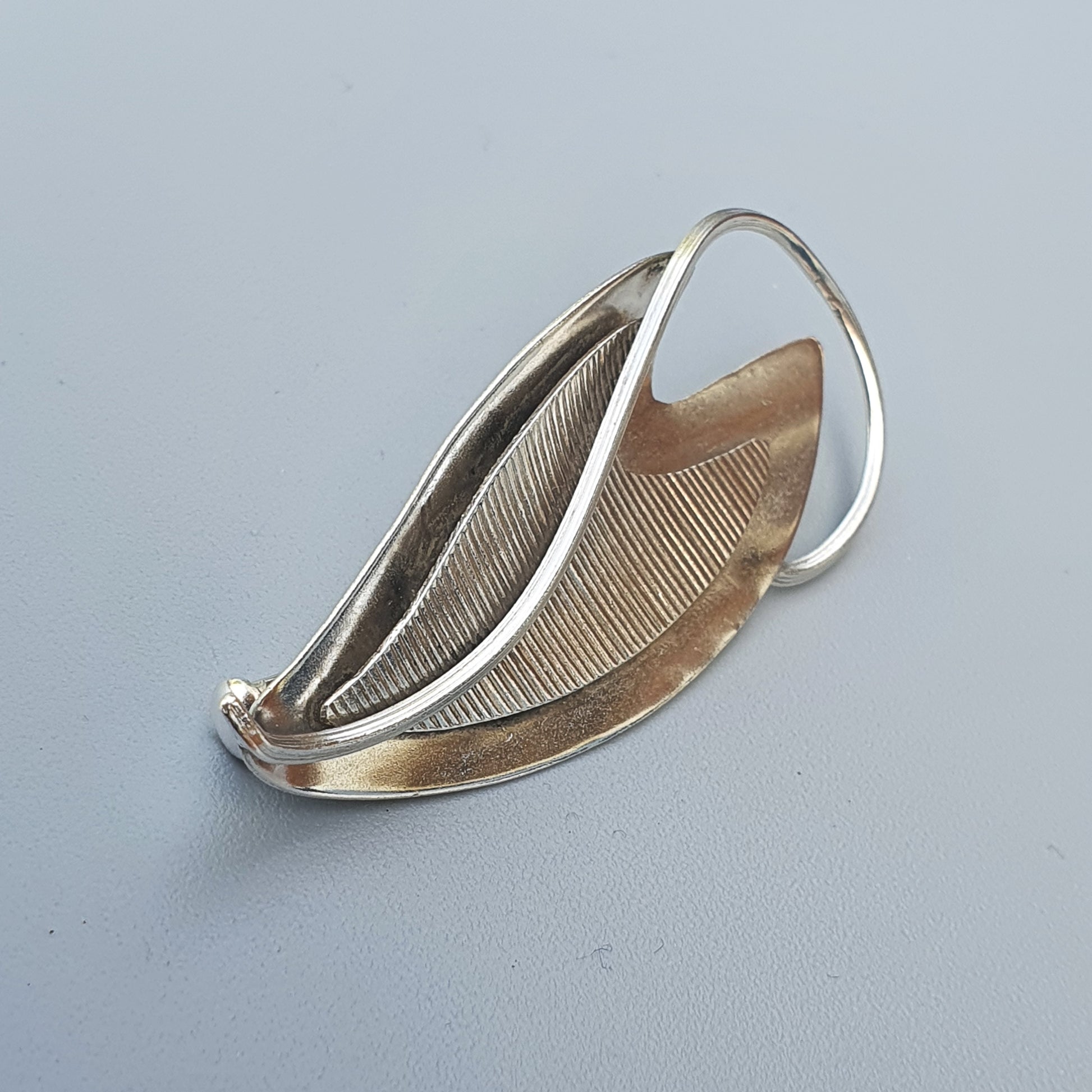 Leaf-shaped silver brooch or pendant with a textured surface and curved edges.