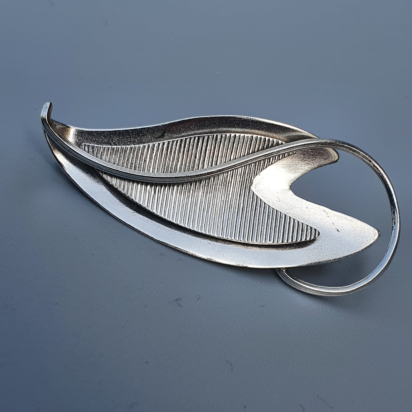 Silver leaf-shaped brooch with a textured, ribbed interior design.