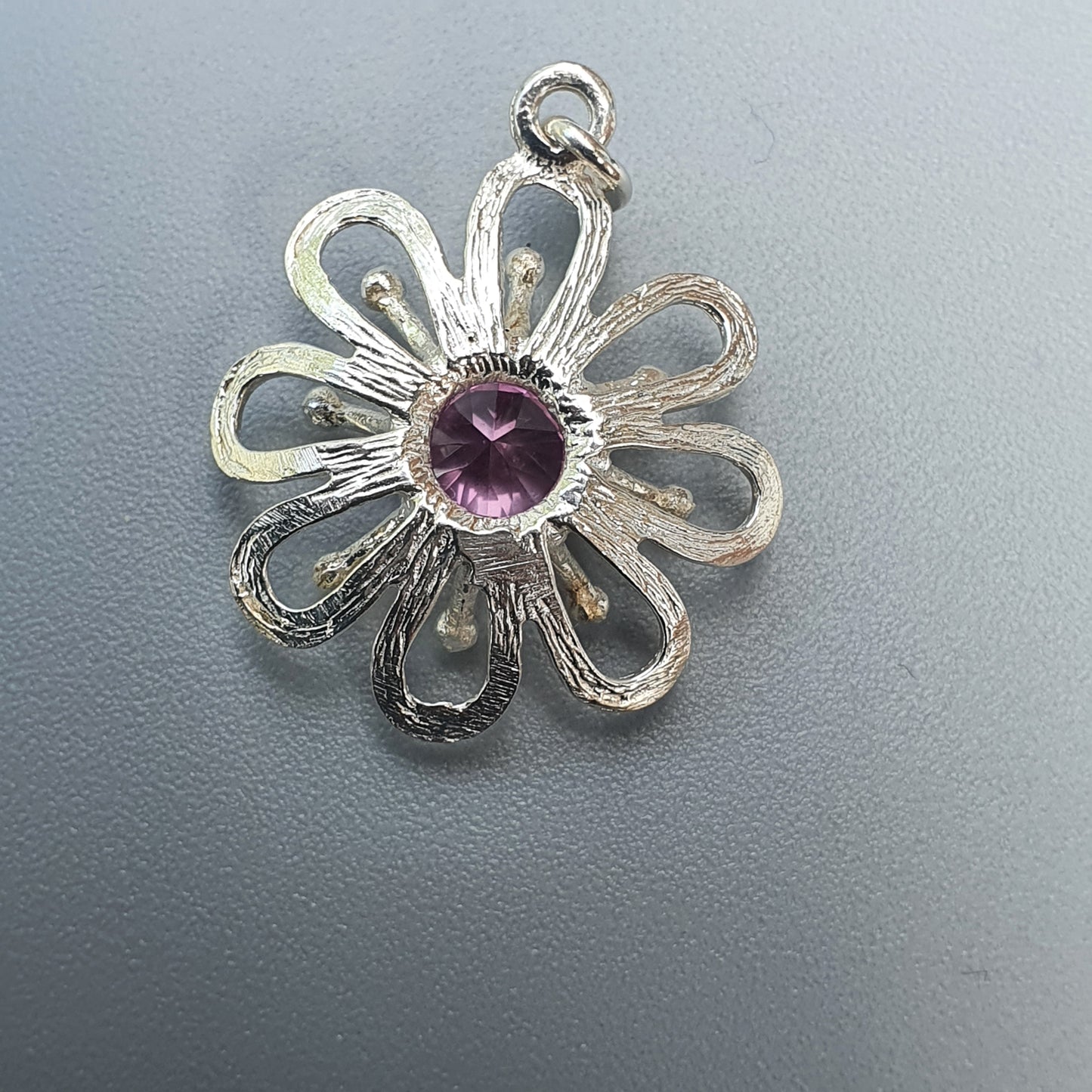 Silver flower-shaped pendant with a purple gemstone center.