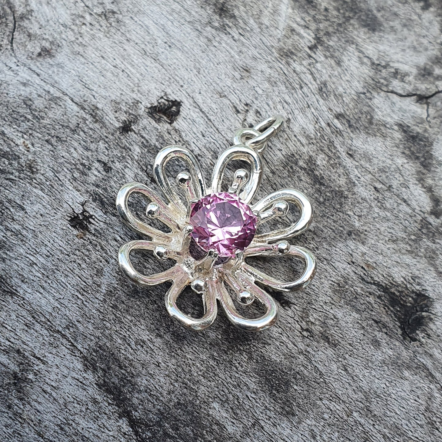 Silver flower-shaped pendant with a pink gemstone center.