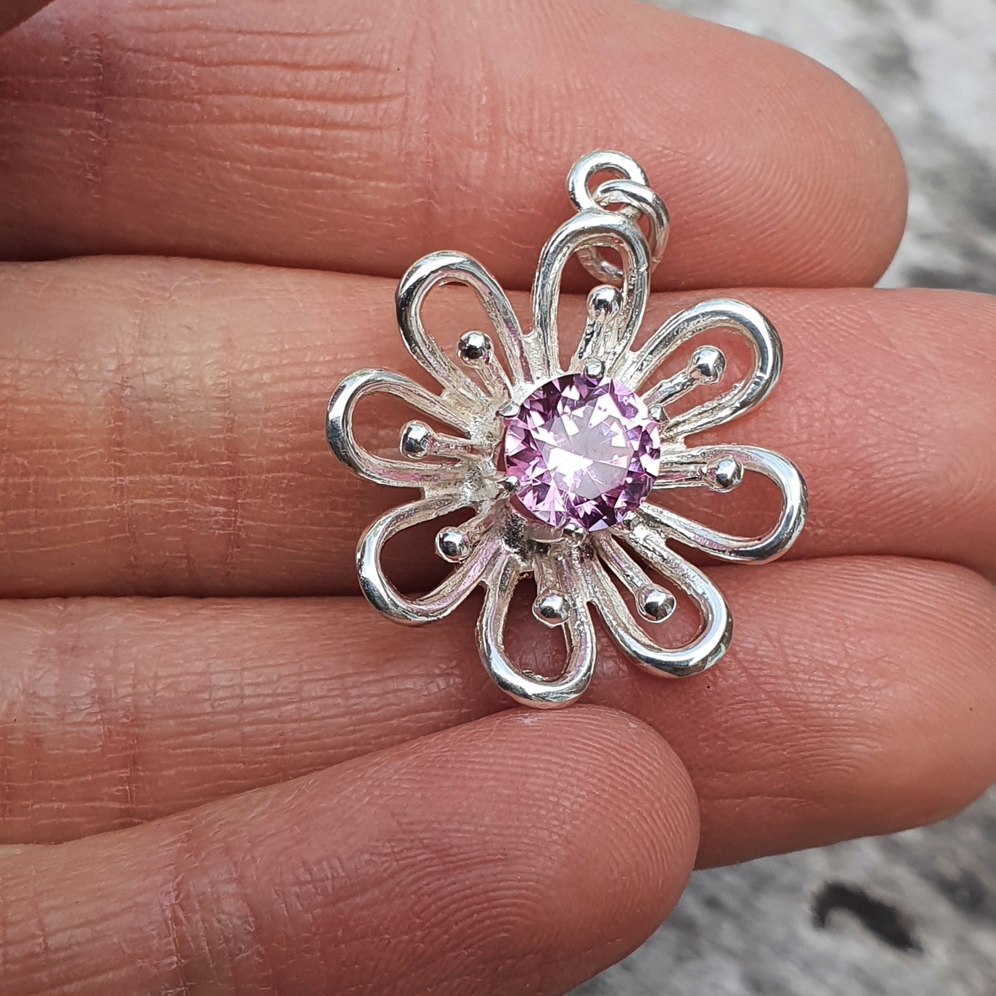 Silver flower-shaped pendant with a pink gemstone center.