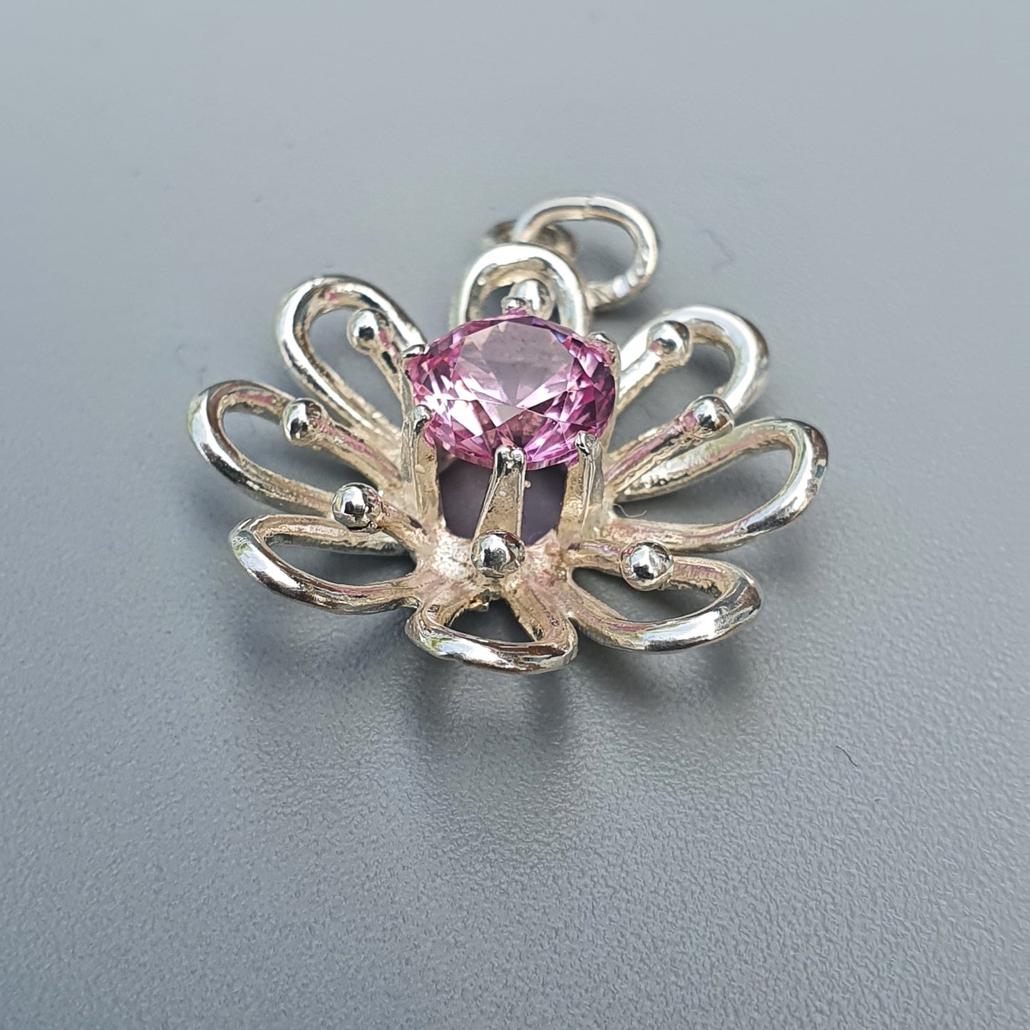 Silver flower-shaped pendant with a pink gemstone center.