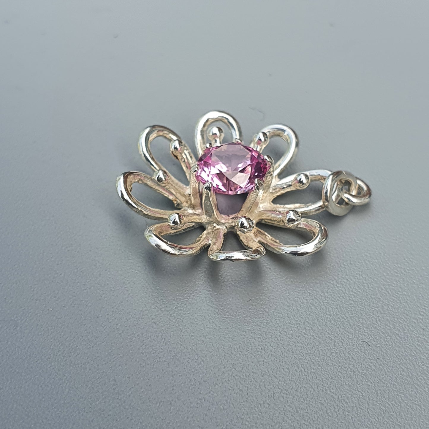 Silver flower-shaped pendant with a pink gemstone center.