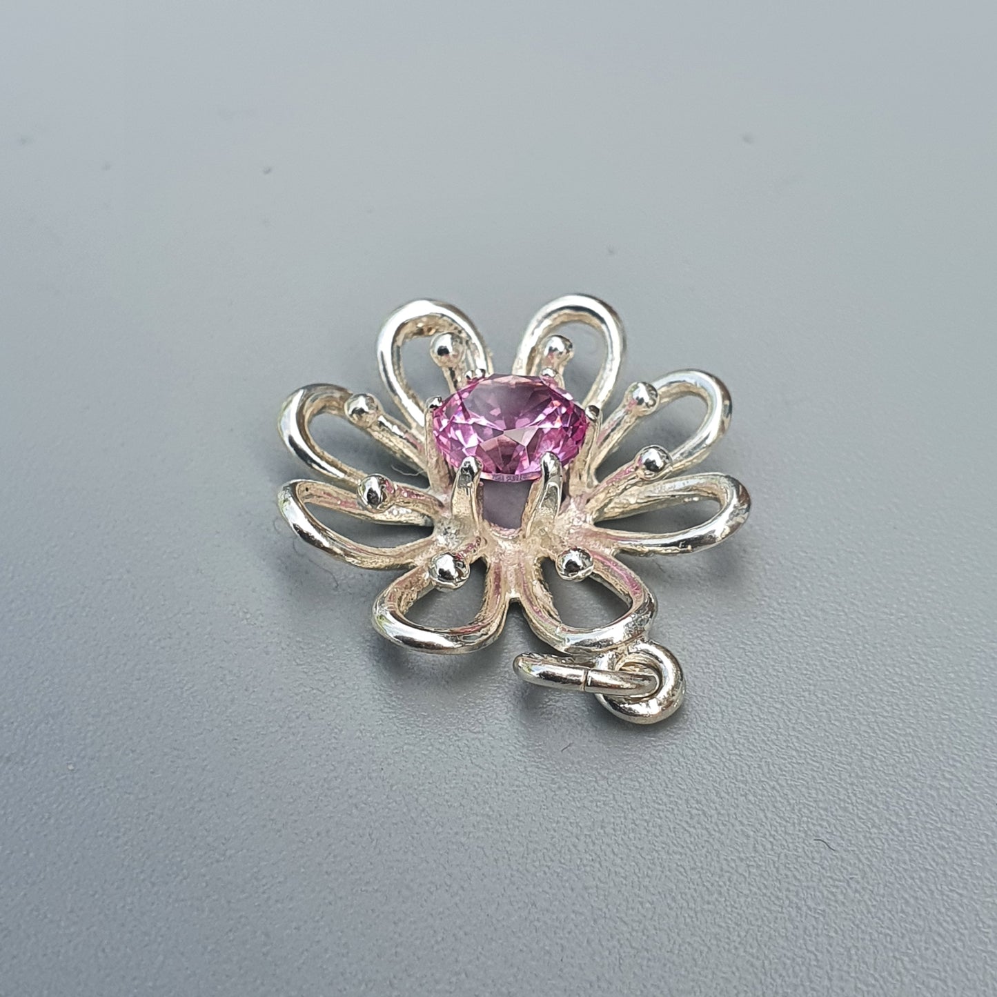 Silver flower-shaped pendant with a pink gemstone center.