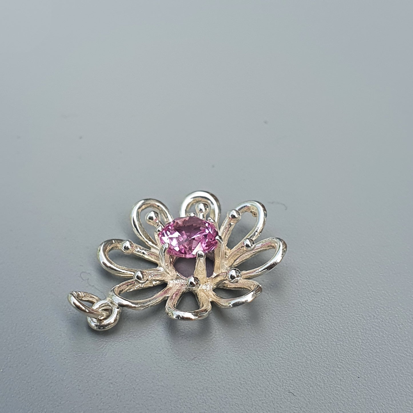 Flower-shaped silver brooch or pendant with a pink gemstone center.