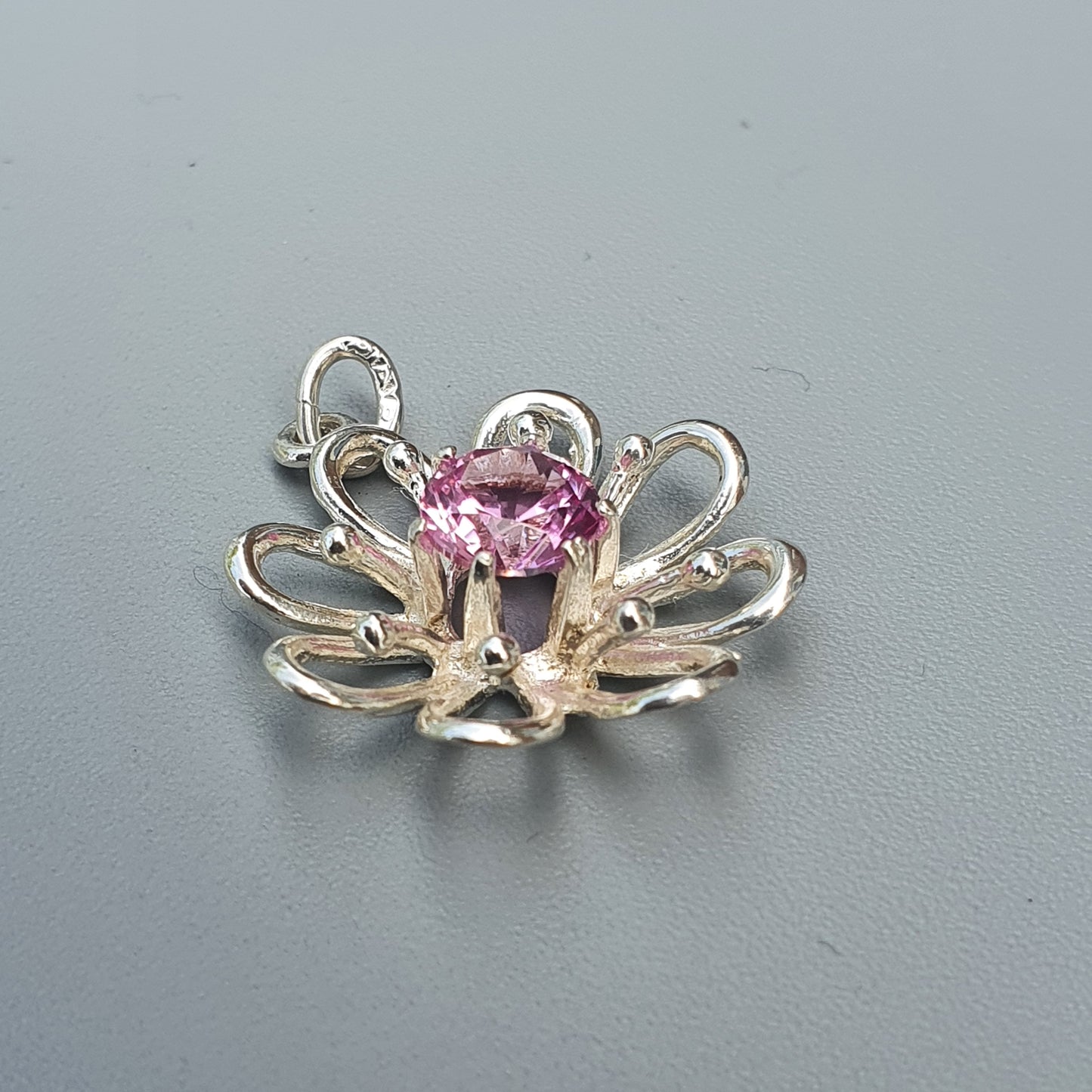 Flower-shaped silver pendant with a pink gemstone center.