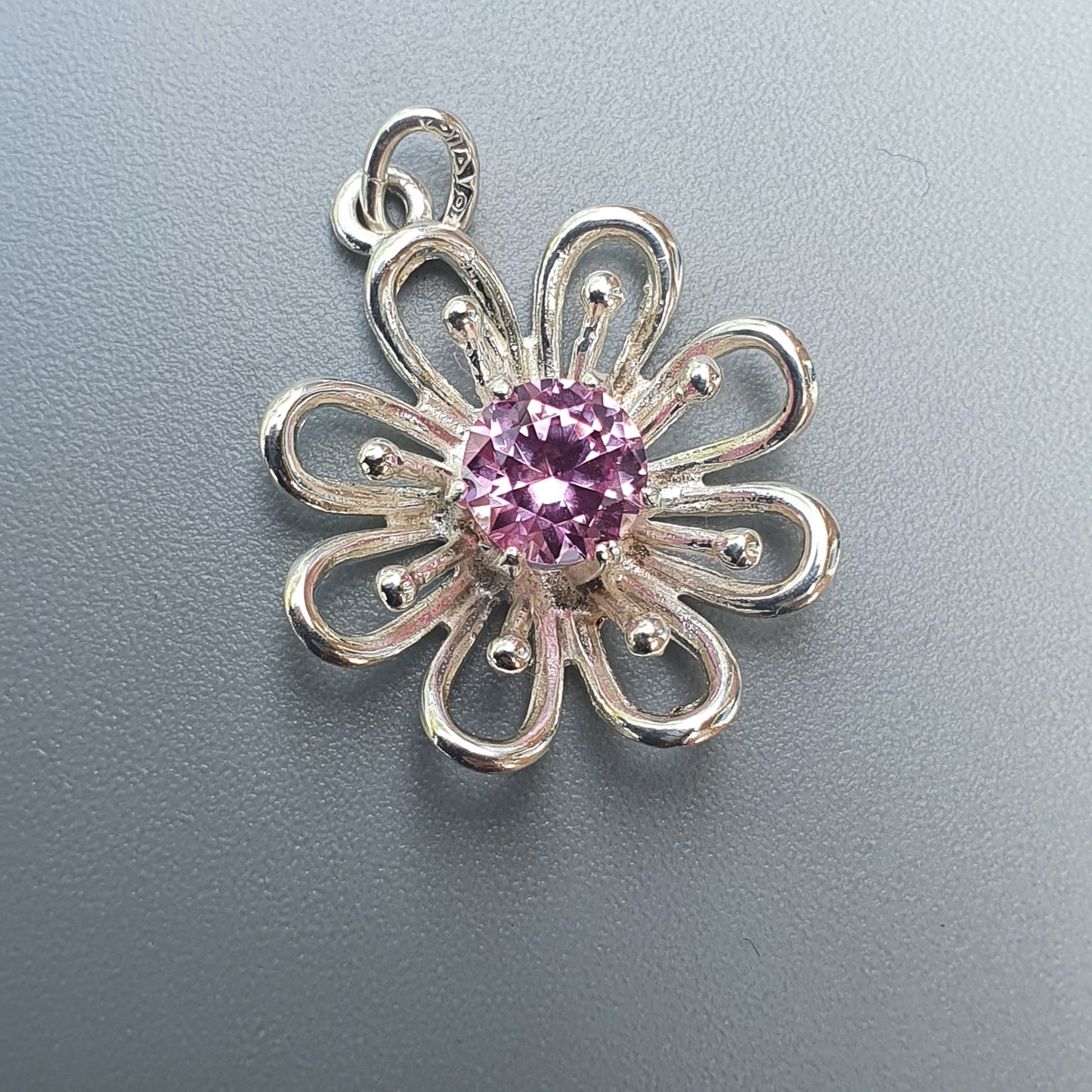 Silver flower-shaped pendant with a pink gemstone center.