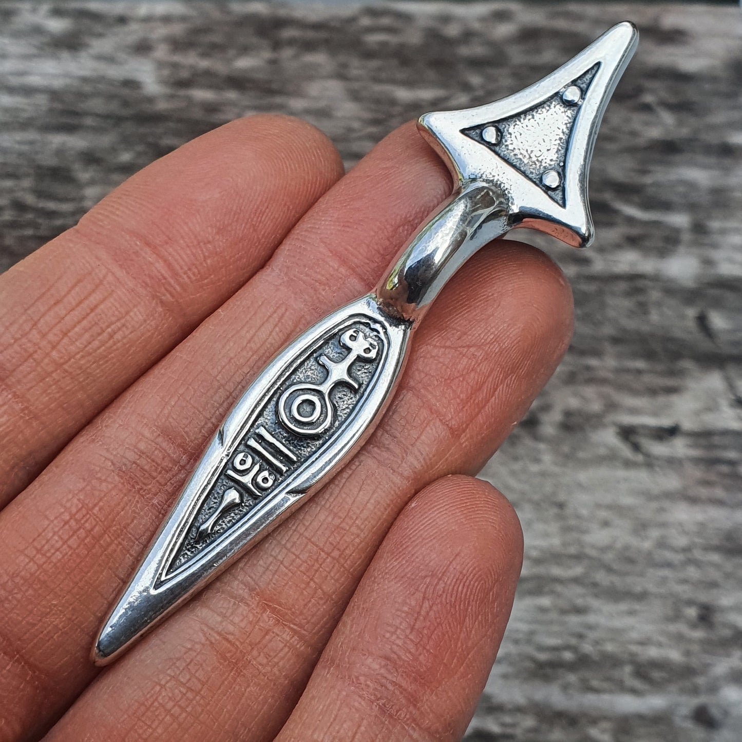 Silver pendant shaped like an elongated arrowhead with intricate engraved designs.