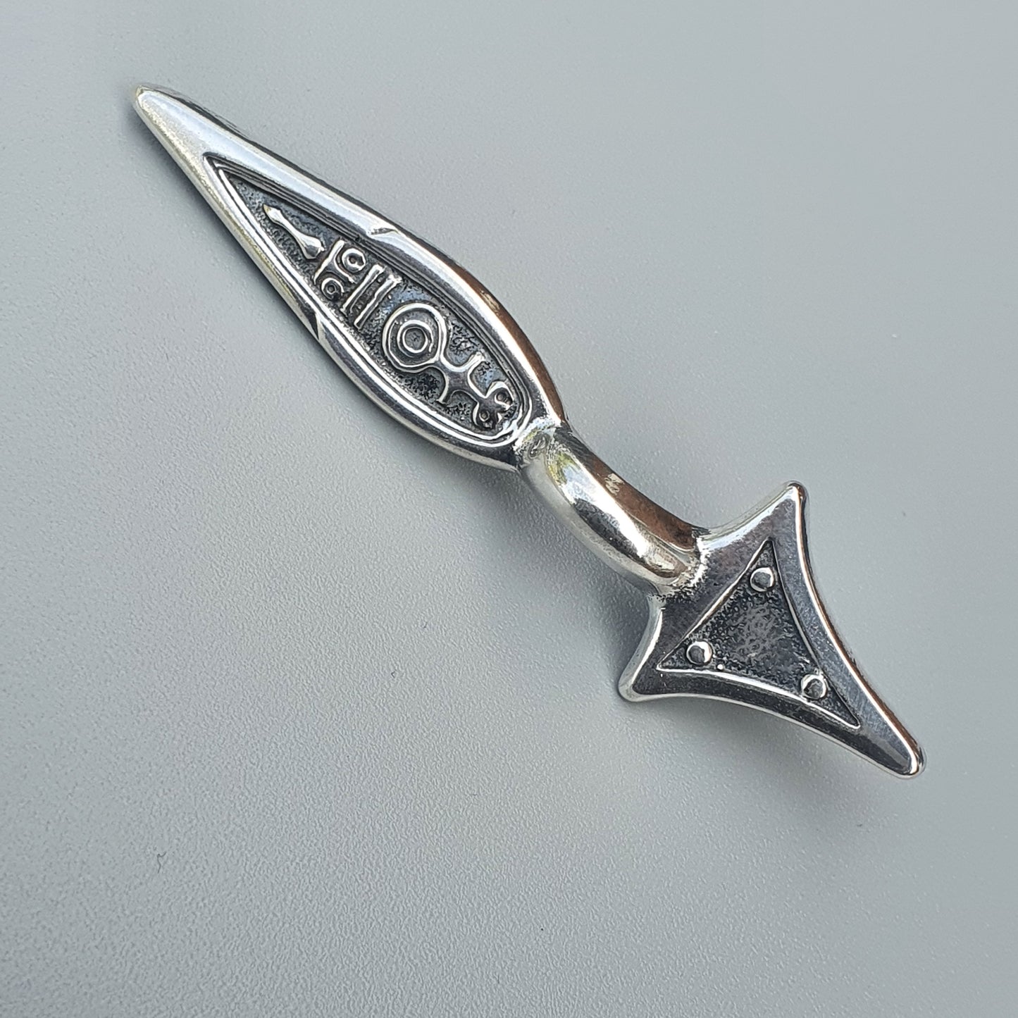 Silver decorative arrowhead-shaped pendant or charm with intricate etched designs.