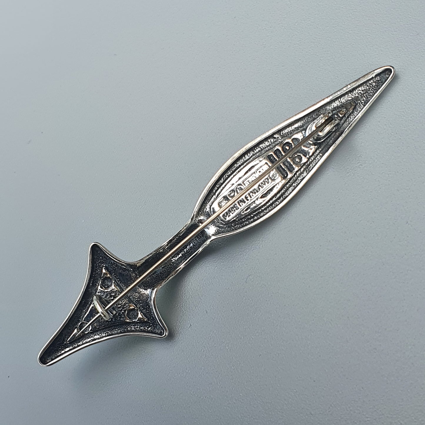 Ornate silver arrow-shaped brooch or pendant with intricate filigree design.