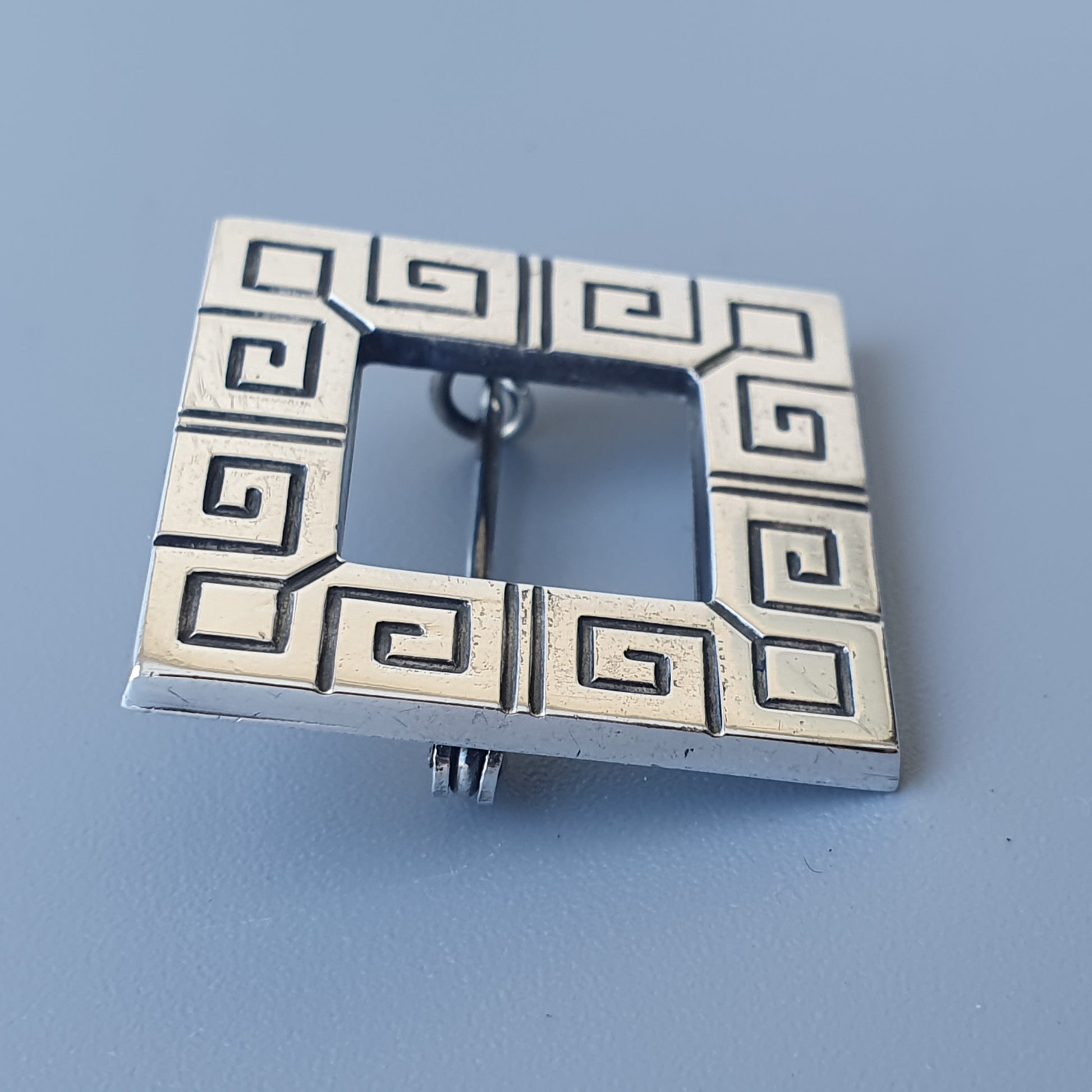 Silver belt buckle with a Greek key pattern design.