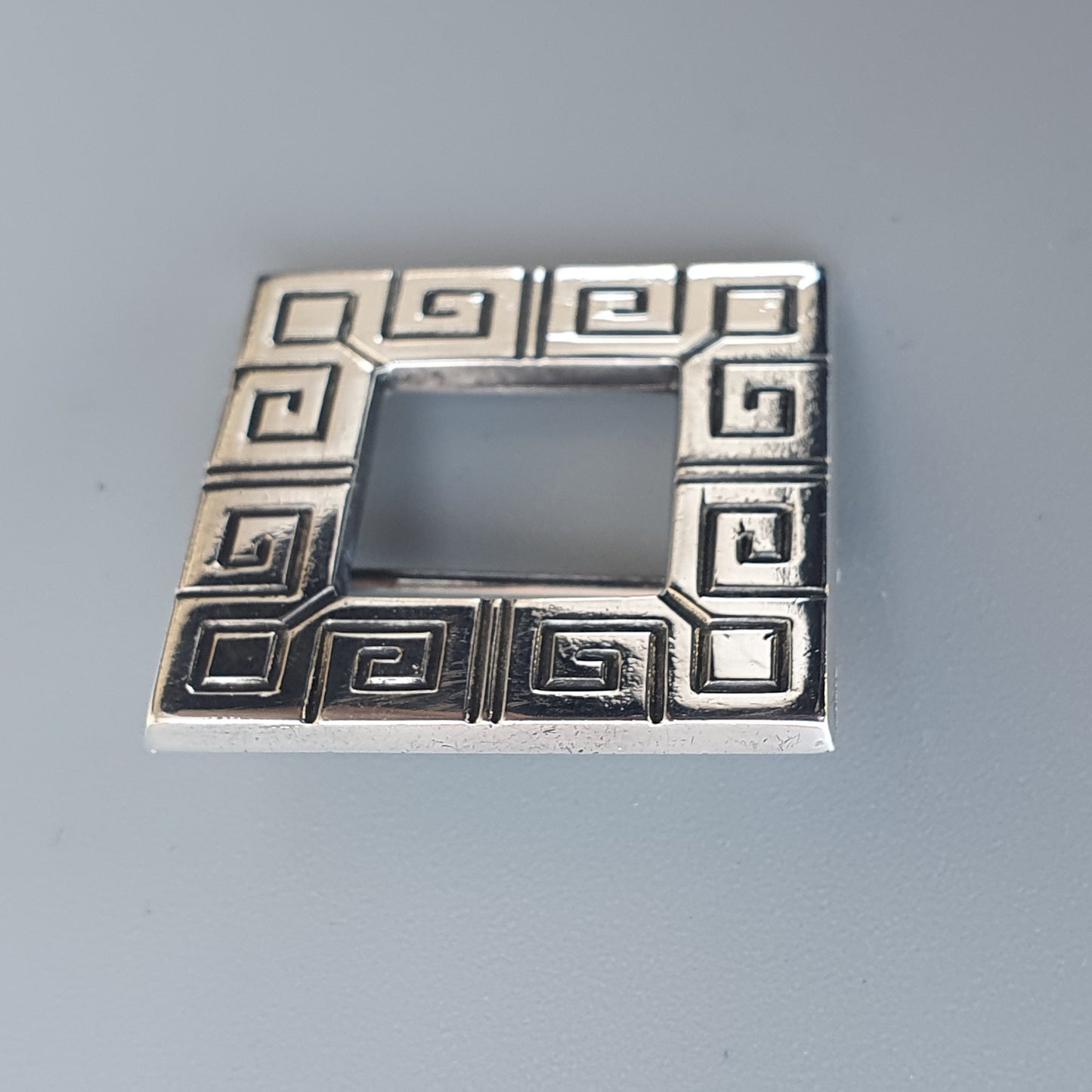 Square silver pendant or brooch with a Greek key pattern border.