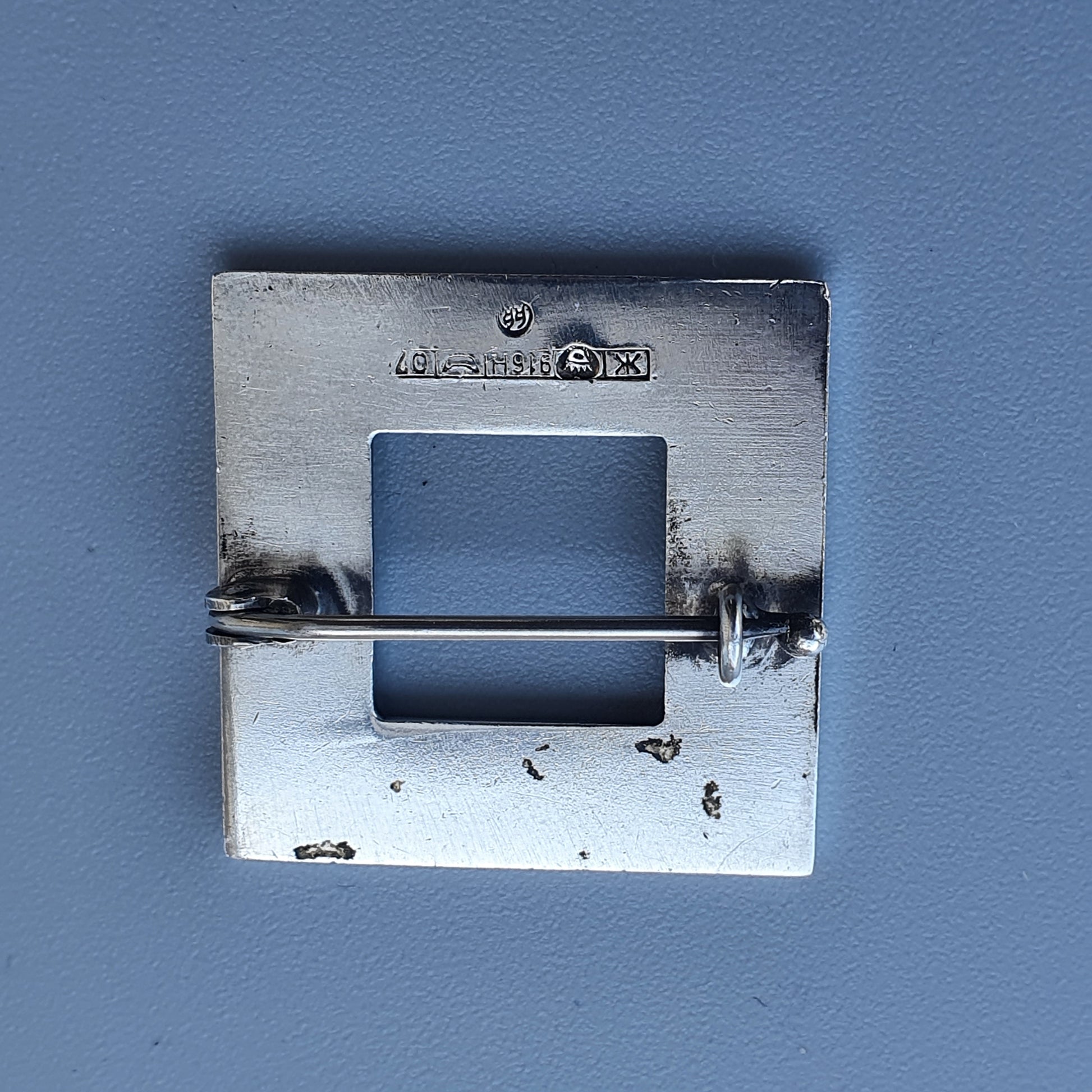 Metal electrical outlet cover plate with a square opening.