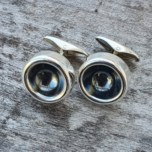 Pair of silver cufflinks with dark circular centers.