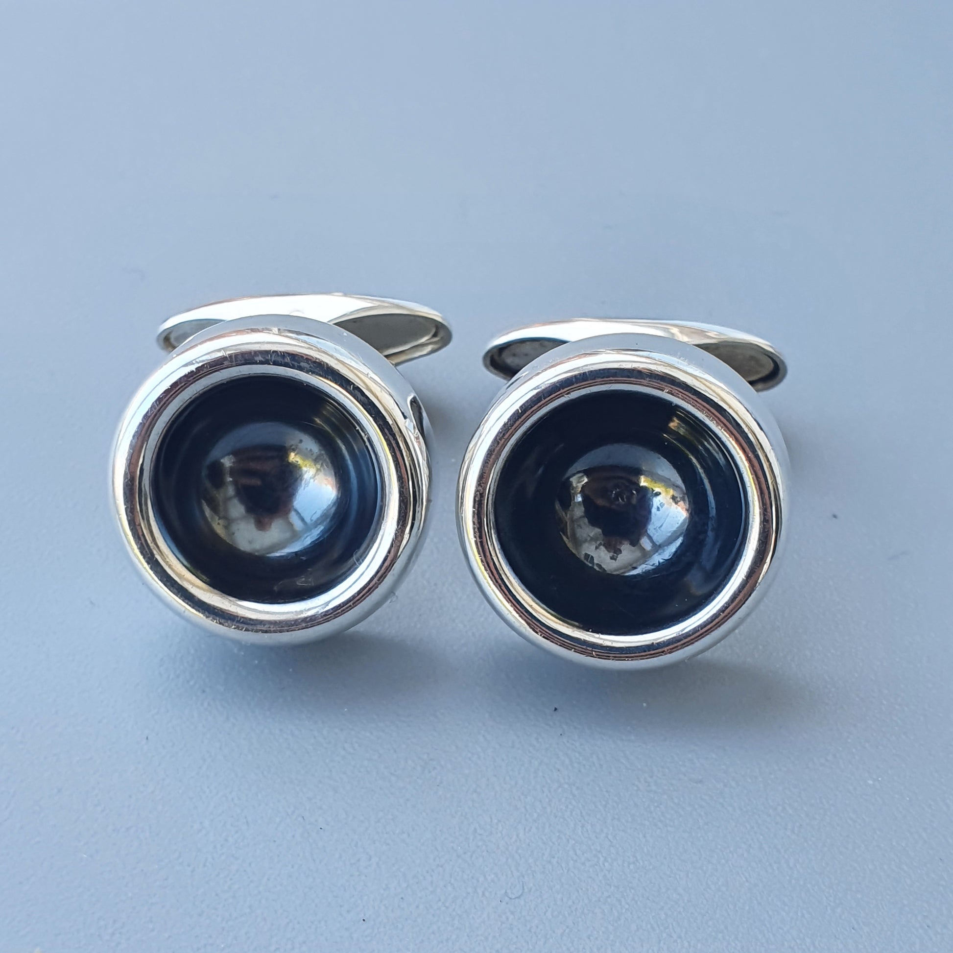 Pair of silver cufflinks with dark circular centers resembling camera lenses.