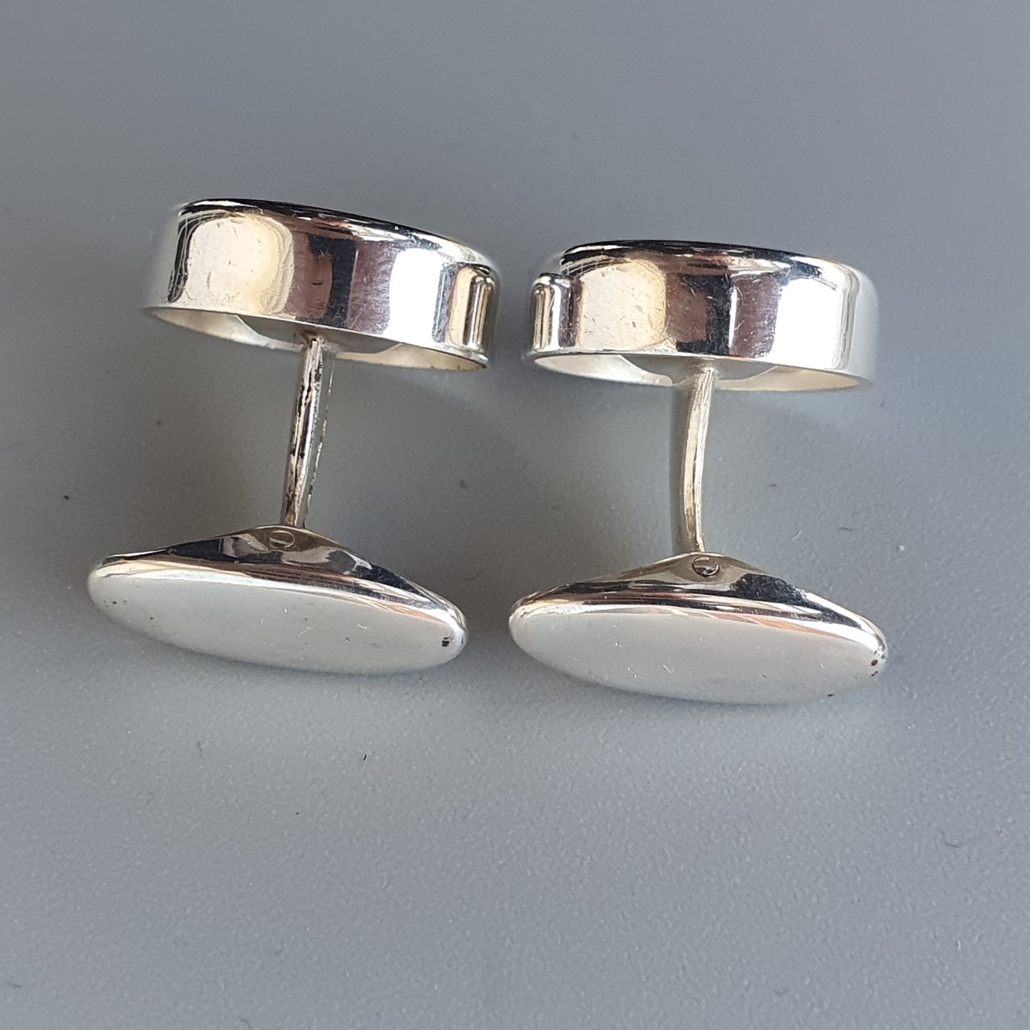 Pair of silver oval cufflinks with smooth, polished surfaces.