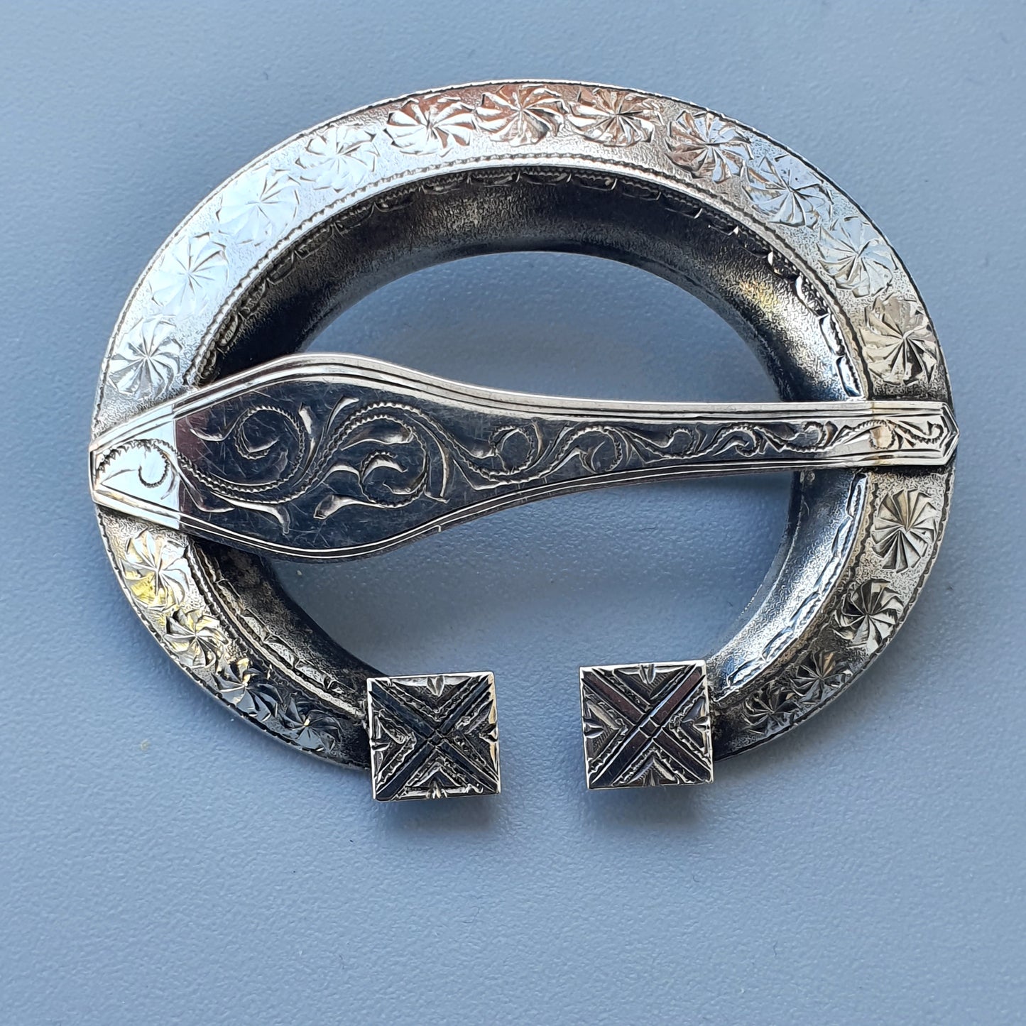 Ornate silver Celtic brooch with intricate engraved designs and open circular shape.