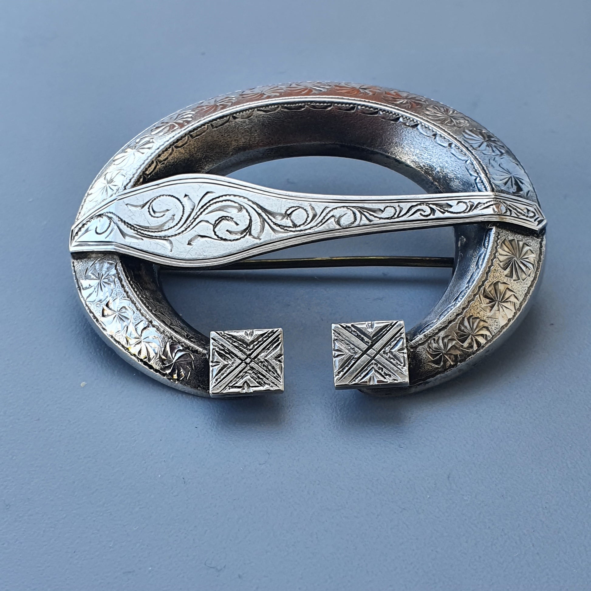 Ornate silver brooch with Celtic-inspired swirling patterns and open circular design.