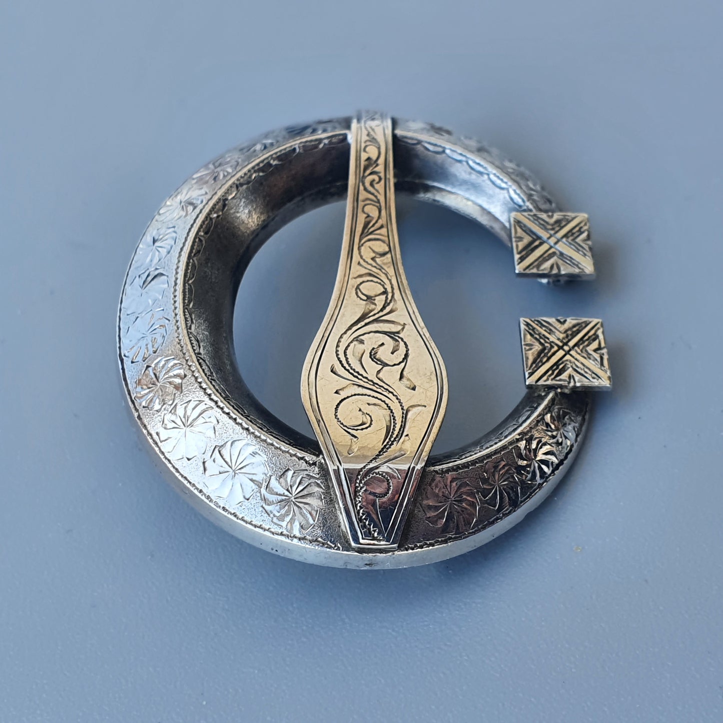 Ornate silver and gold Celtic brooch with intricate engraved designs.