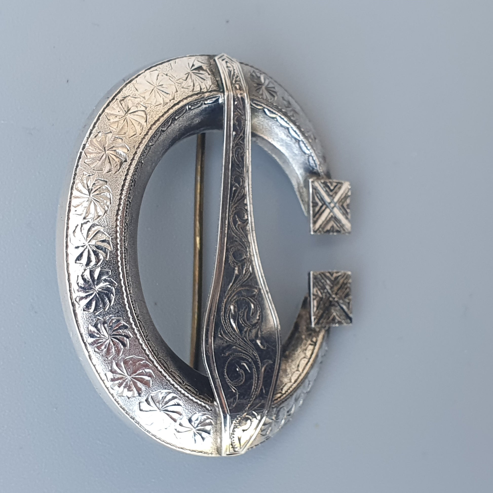 Silver Celtic-style brooch with intricate engraved patterns and a pin closure.