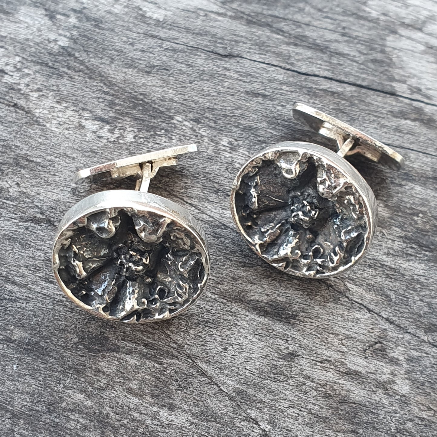 Pair of circular silver cufflinks with intricate floral or star-like designs.