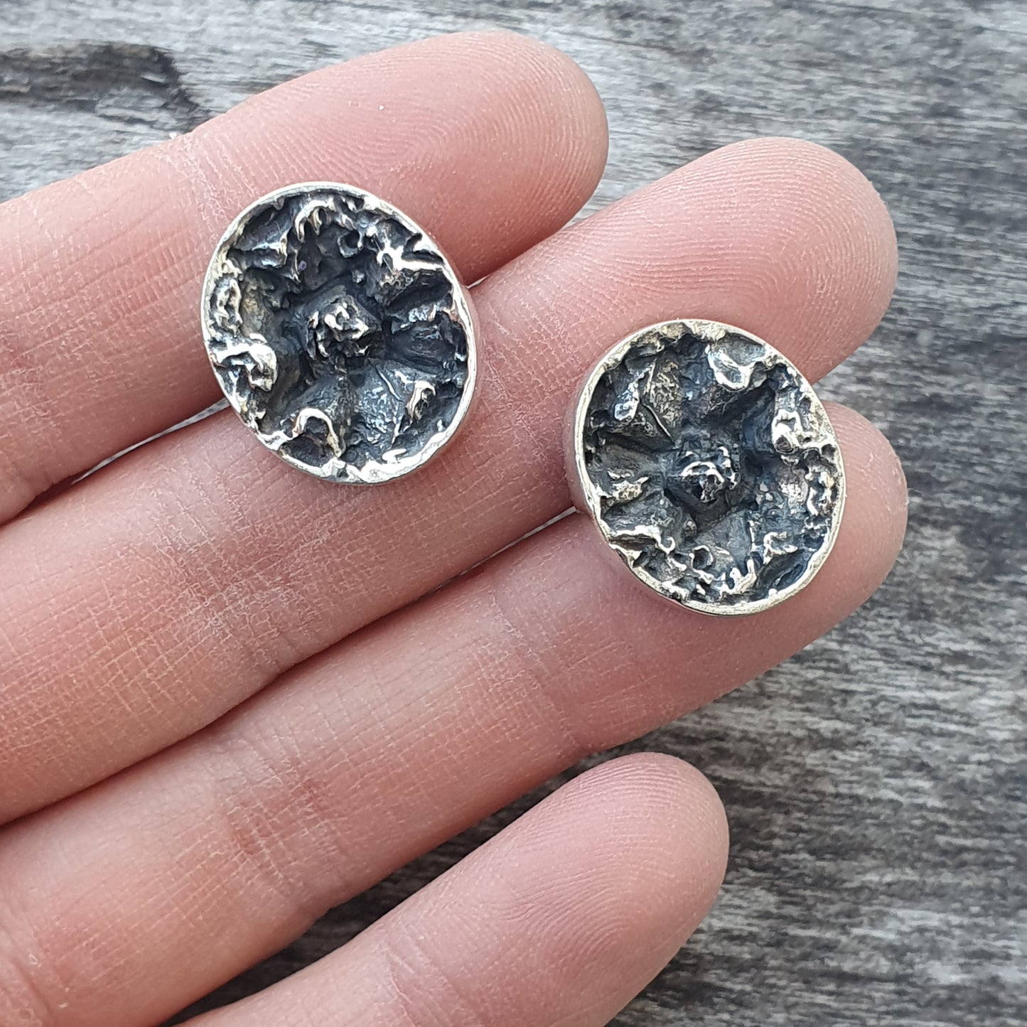 Pair of circular silver earrings with textured, organic-looking surfaces.