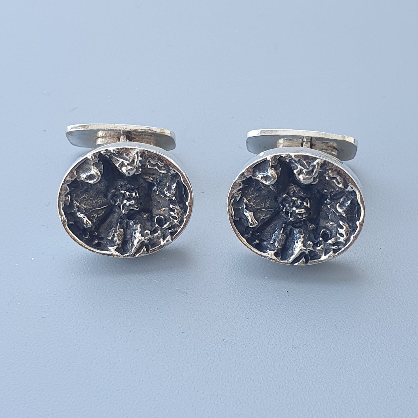 Pair of oval silver cufflinks with textured, dark-colored centers.