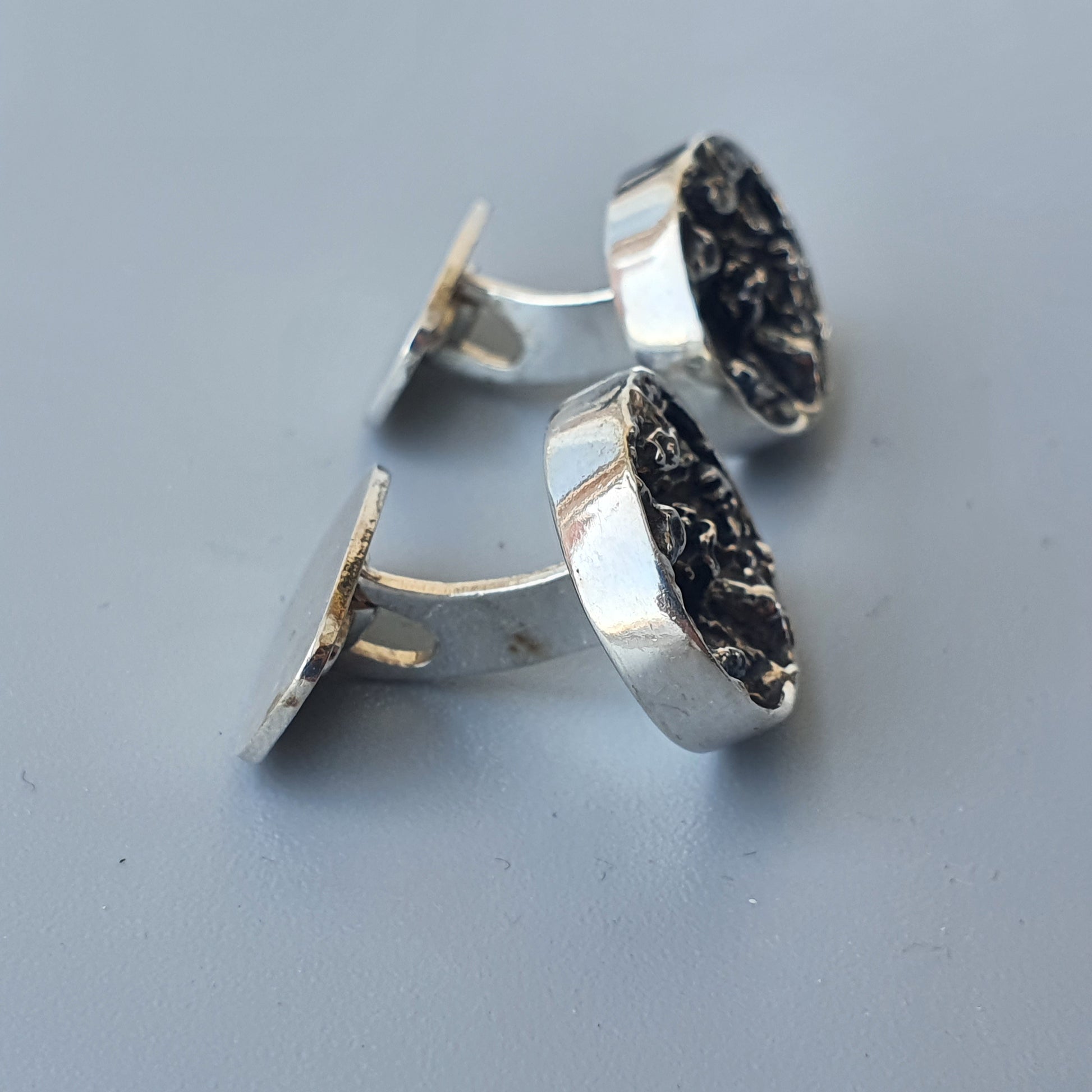 Pair of silver cufflinks with dark, textured circular faces.