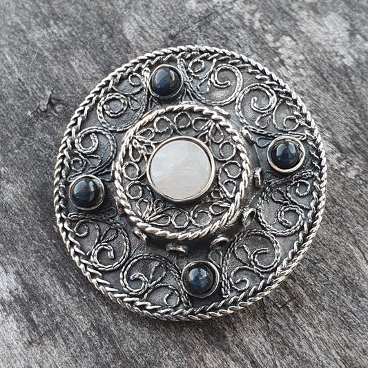 Ornate silver brooch with intricate filigree design and dark gemstones.