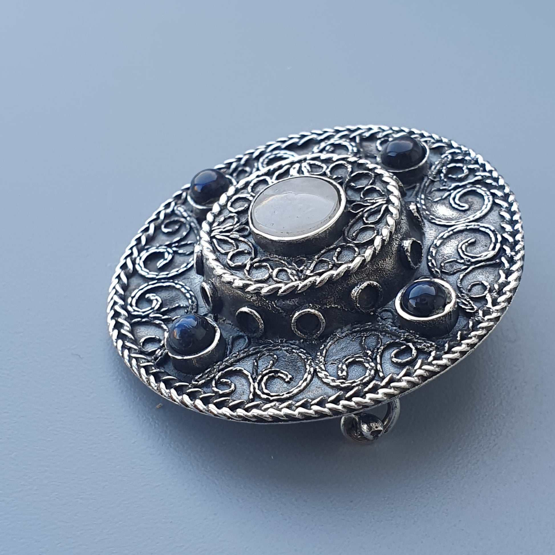 Ornate silver brooch with intricate filigree patterns and blue gemstones.