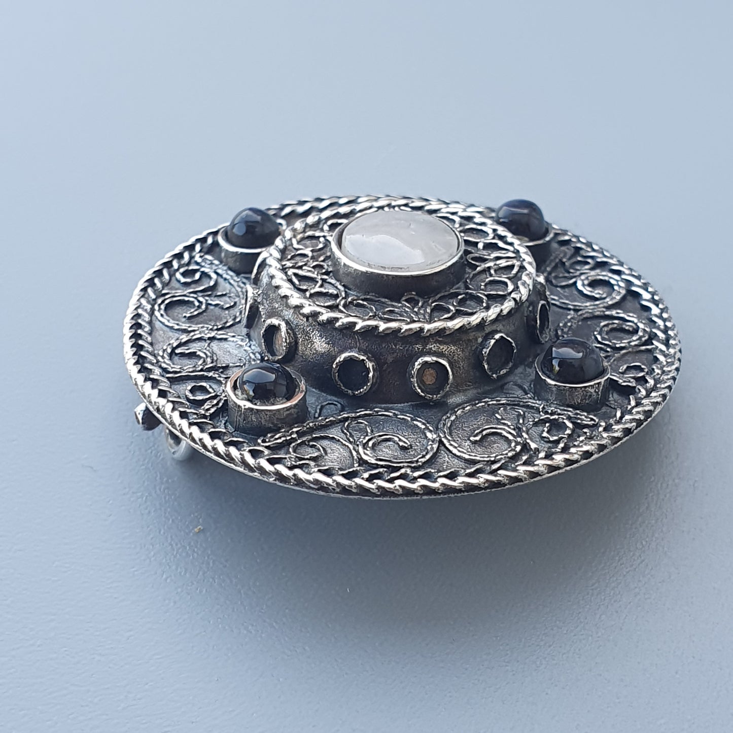 Ornate silver brooch or pendant with intricate filigree and gemstone details.