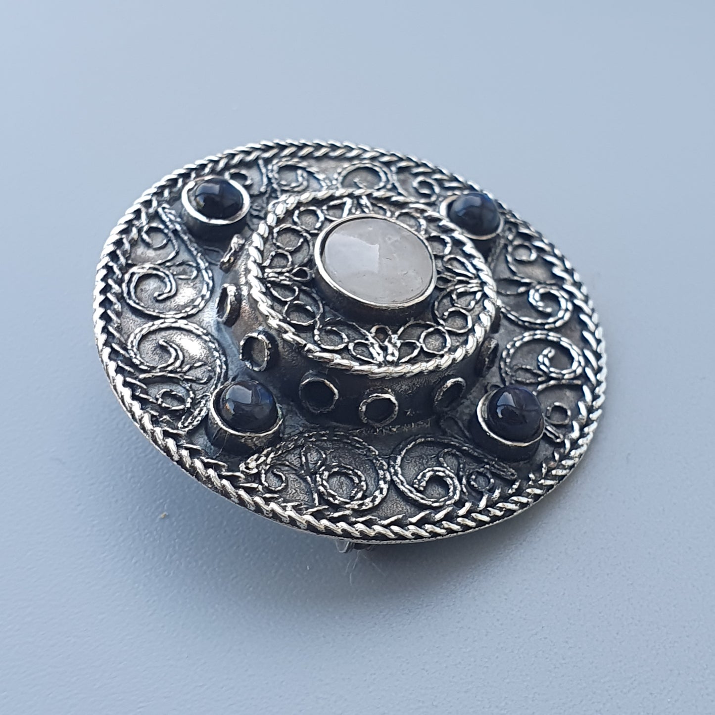 Ornate silver brooch or pendant with intricate filigree designs and a central gemstone.