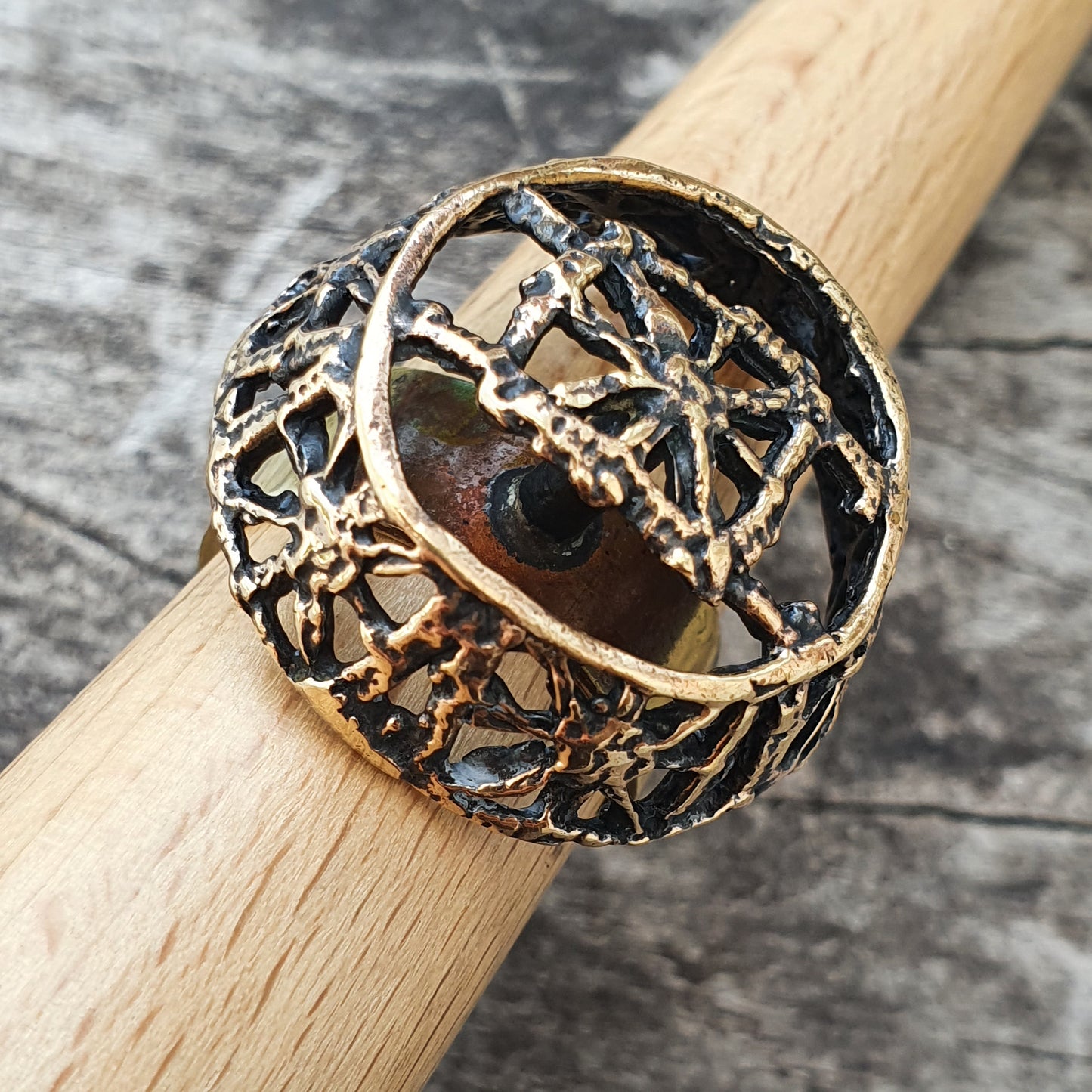 Ornate gold-toned ring with an intricate web-like design encasing a dark stone or bead.