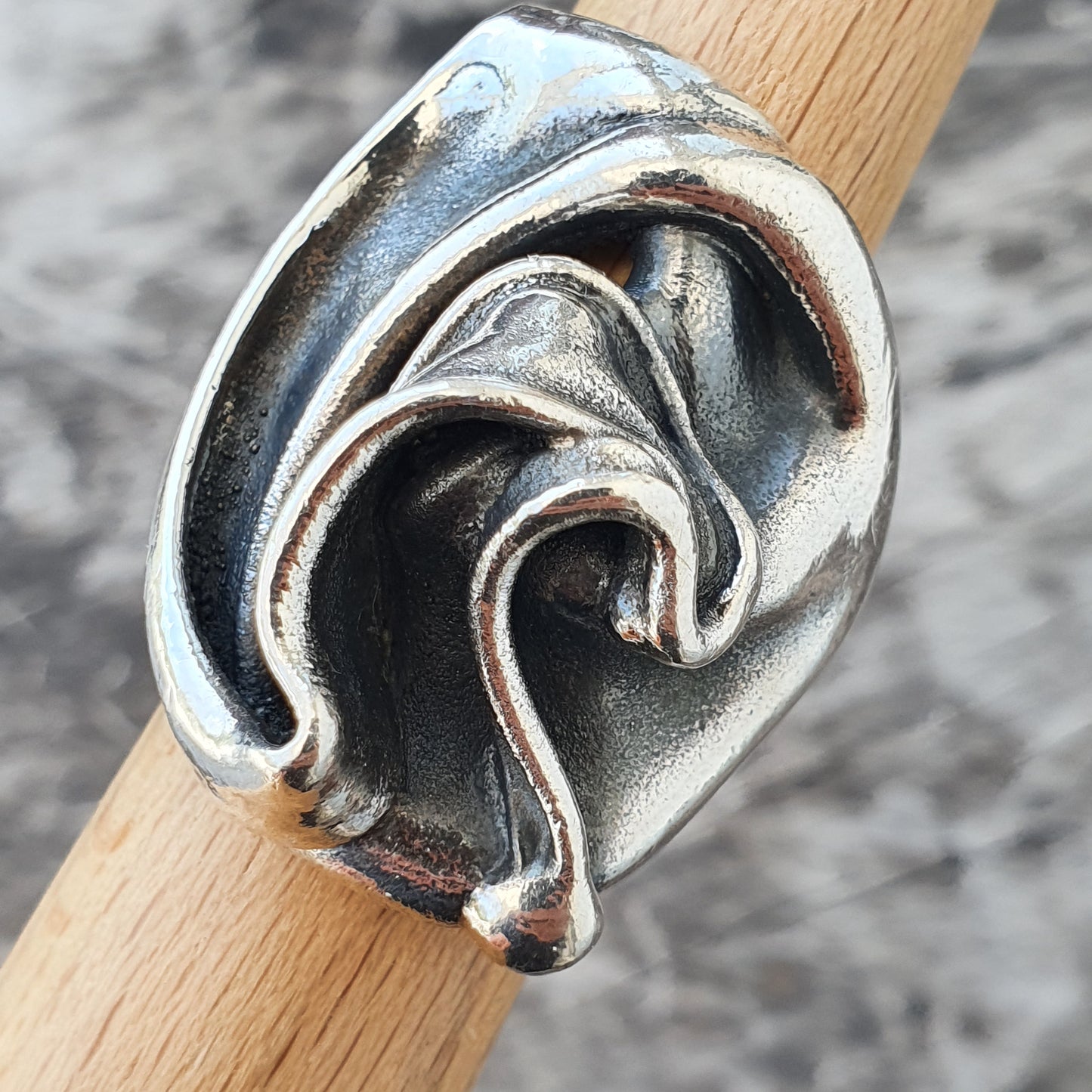 Silver ring with a swirling, abstract design resembling waves or folds.