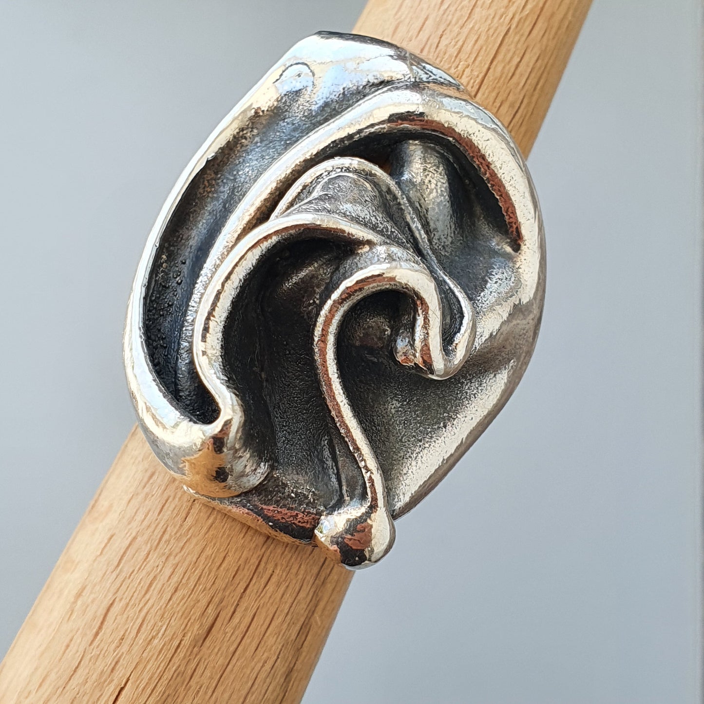 Silver ring with an abstract, swirling design resembling waves or fluid motion.