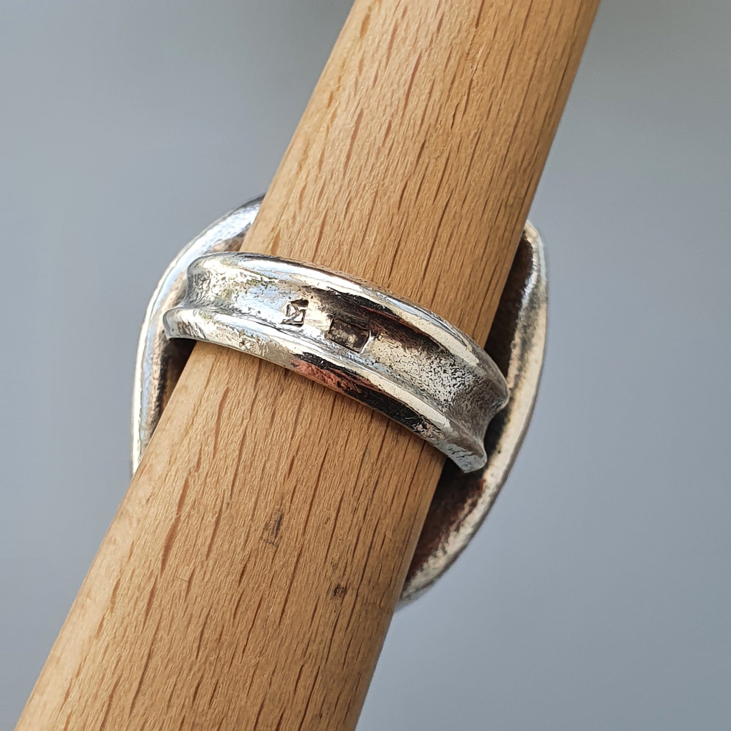 Silver ring with a unique overlapping design wrapped around a wooden dowel.