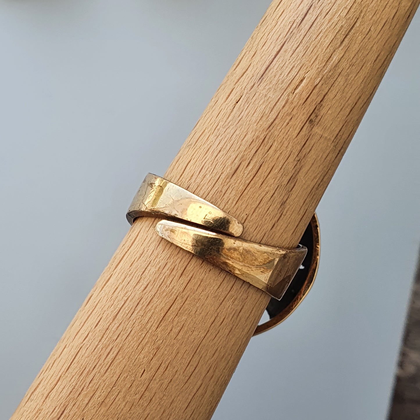 Gold ring with a twisted or ribbon-like design wrapped around a wooden cylinder.