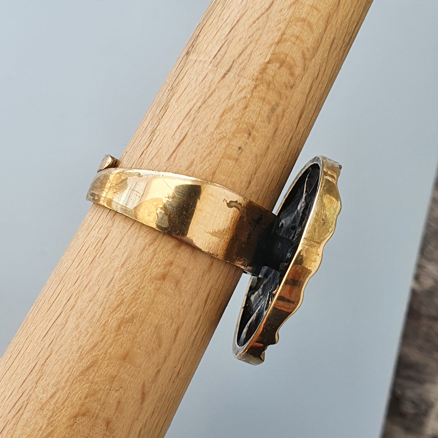 Gold ring with a black stone or enamel accent wrapped around a wooden dowel.