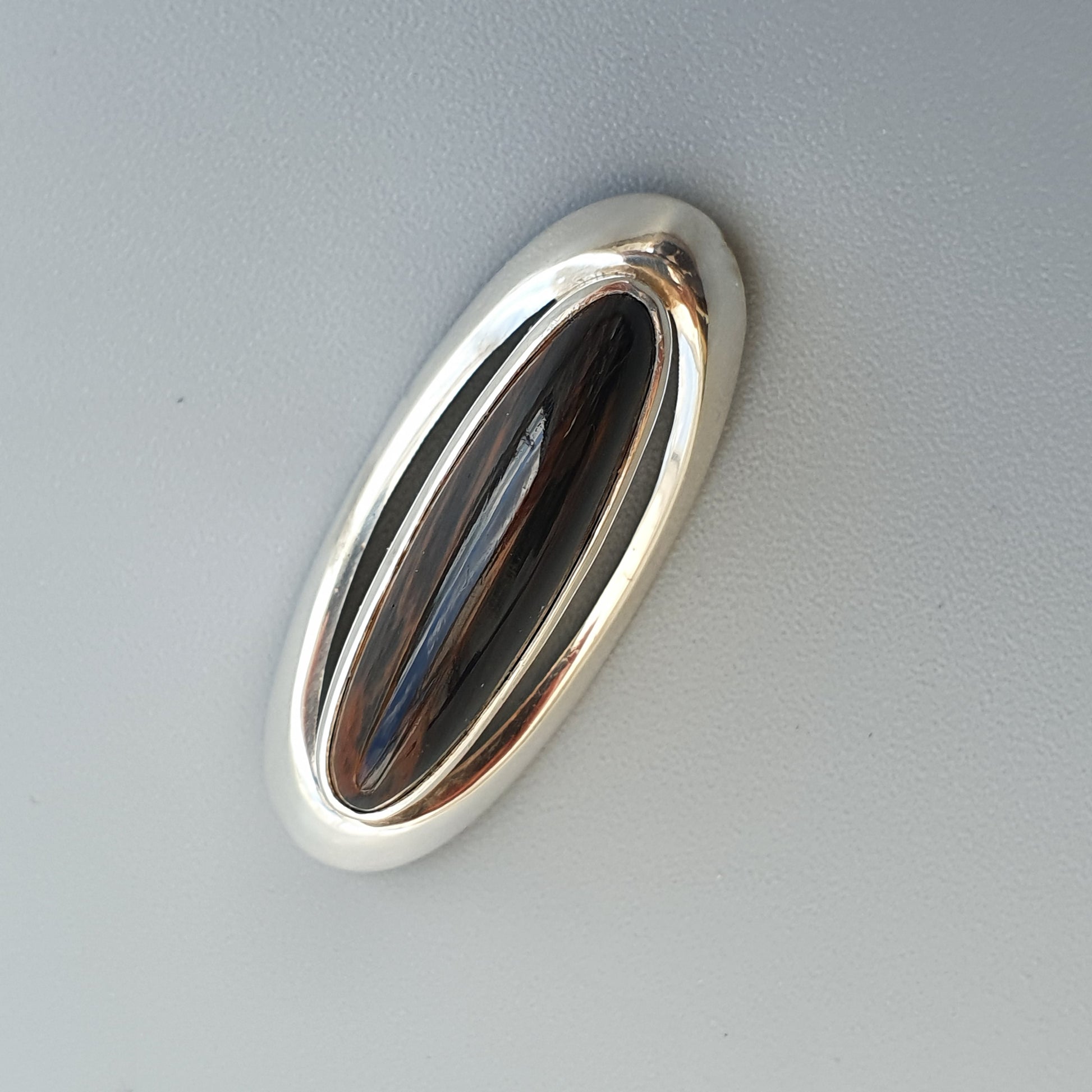 Oval-shaped silver car door handle with a dark inset panel.