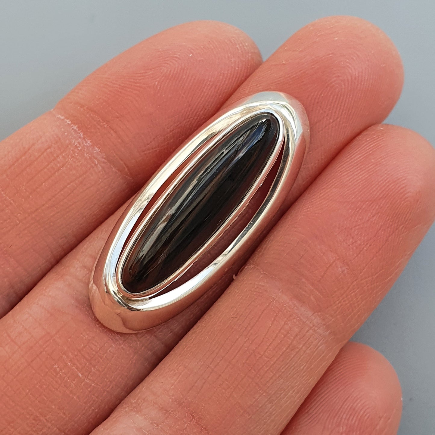 Silver ring with an elongated oval black stone or gem inset.