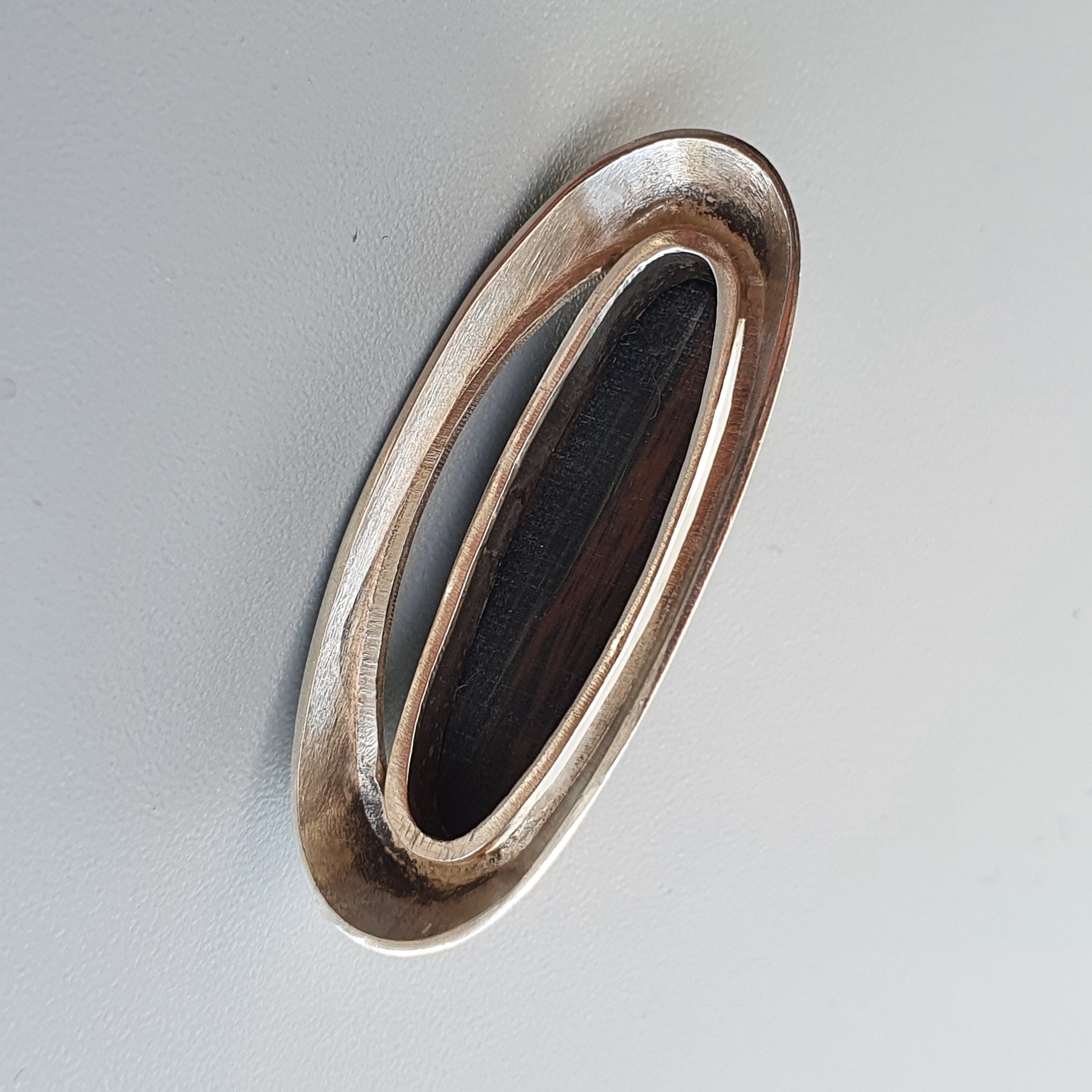 Oval-shaped metallic object with a dark central opening, likely a door handle or drawer pull.