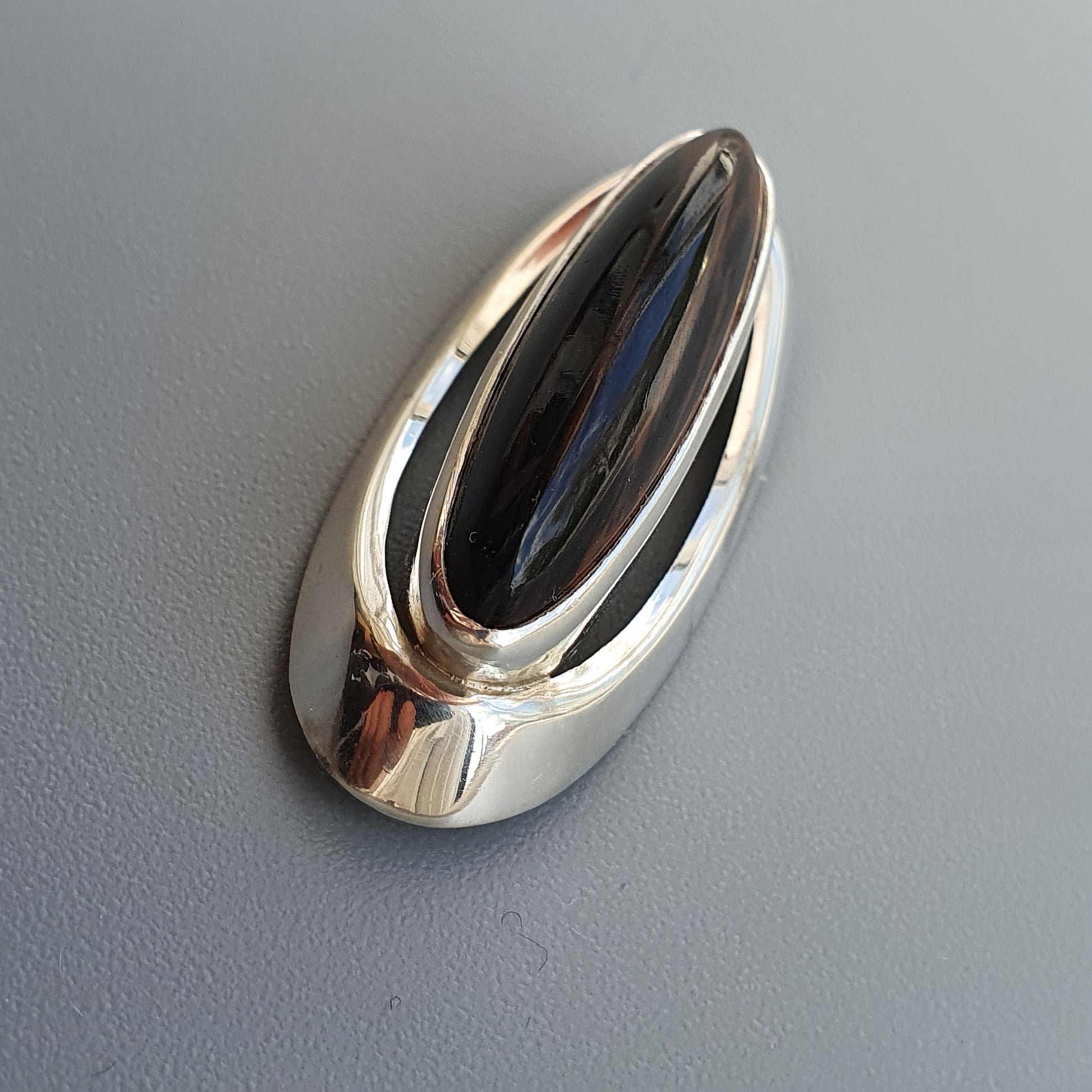 Shiny silver-colored oval brooch or pendant with a dark inset.