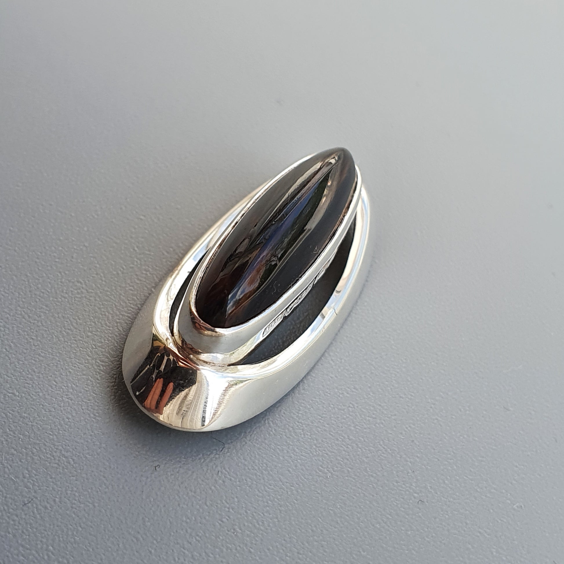 Sleek, oval-shaped silver pendant or jewelry piece with a curved, elongated opening.