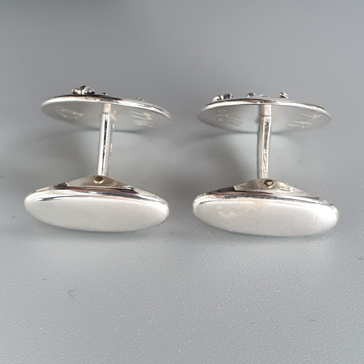 Pair of oval silver cufflinks with smooth, polished surfaces.