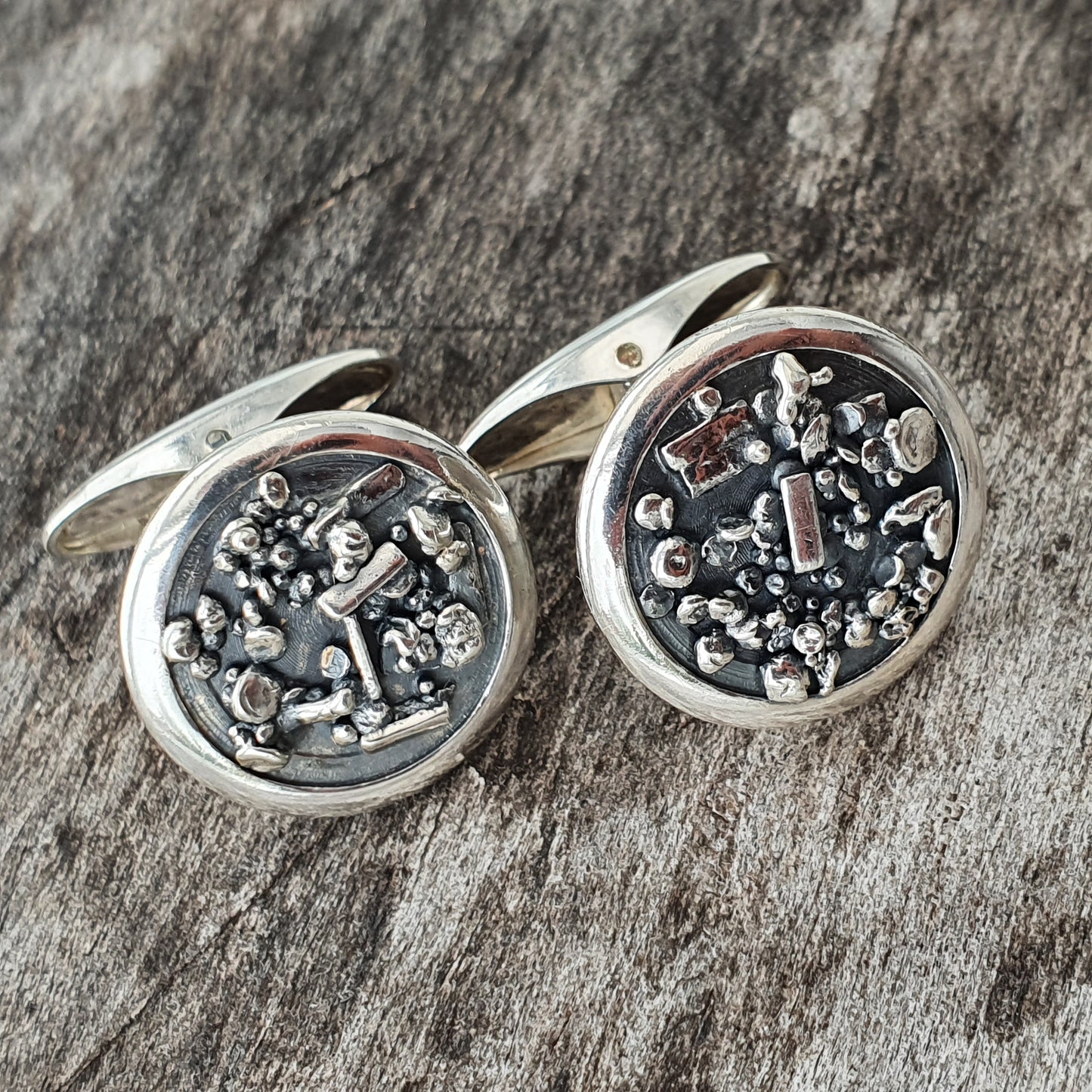 Pair of silver cufflinks with intricate circular designs featuring crosses and small metallic elements.