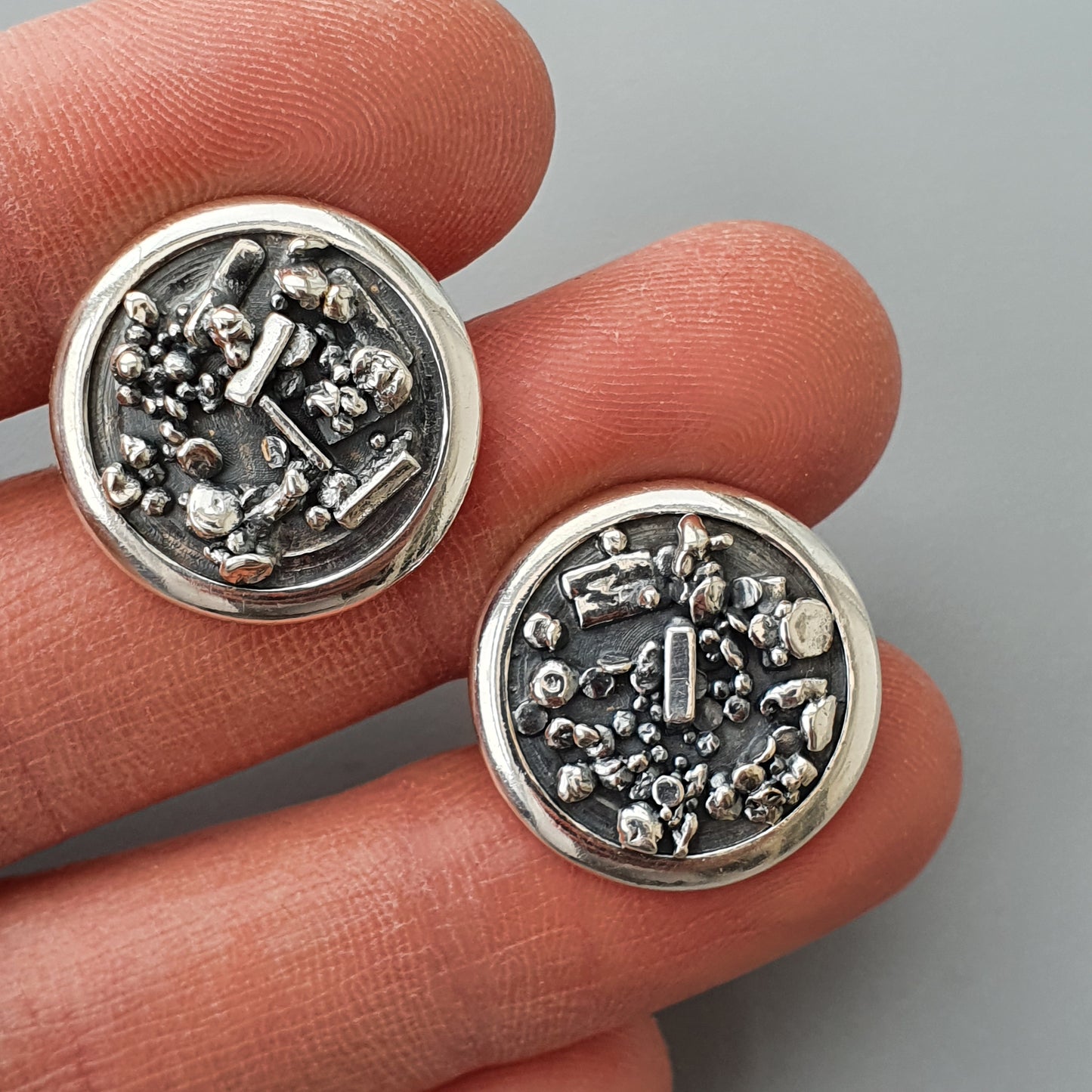 Pair of circular silver earrings with intricate metallic designs.