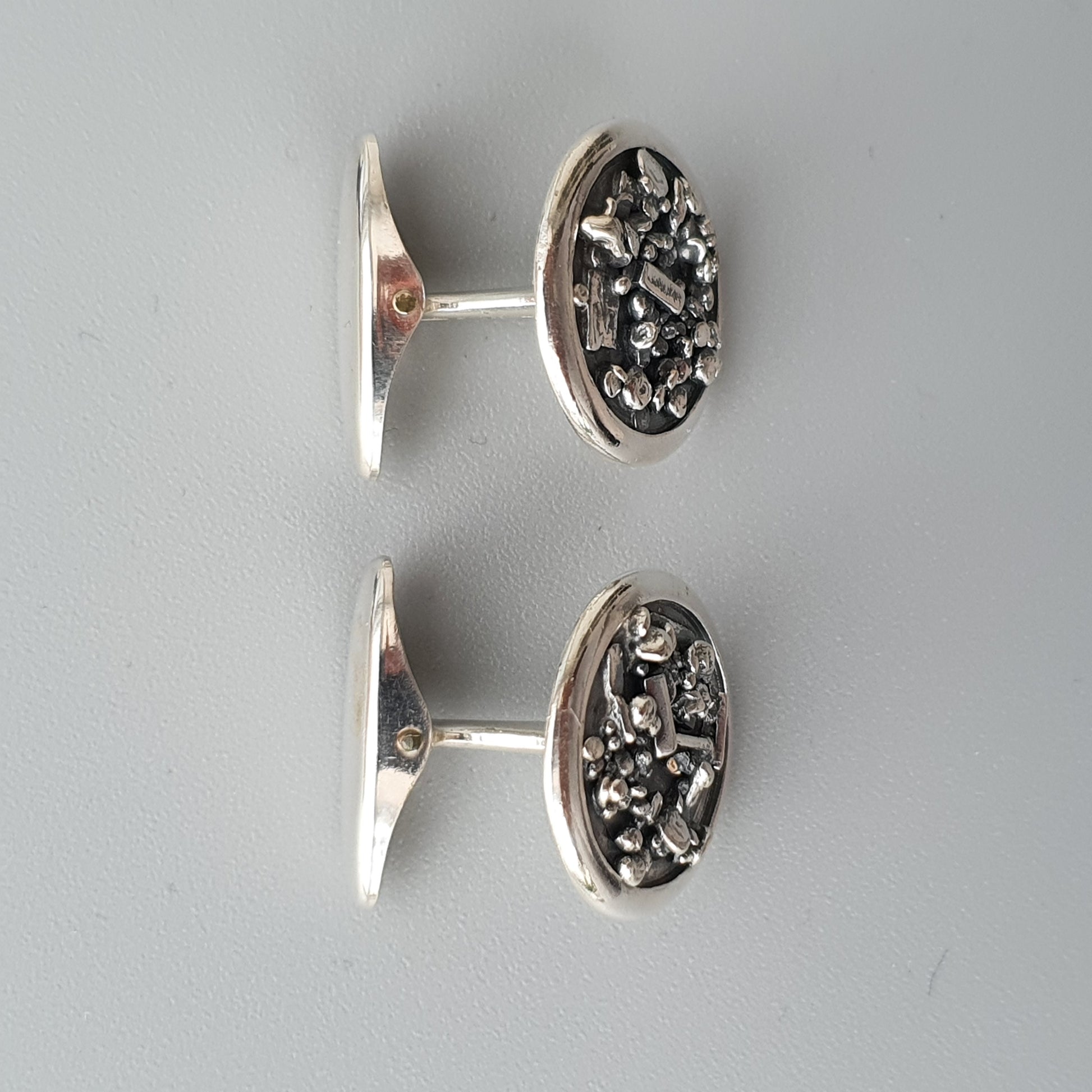 Pair of oval silver cufflinks with textured, metallic designs on their faces.