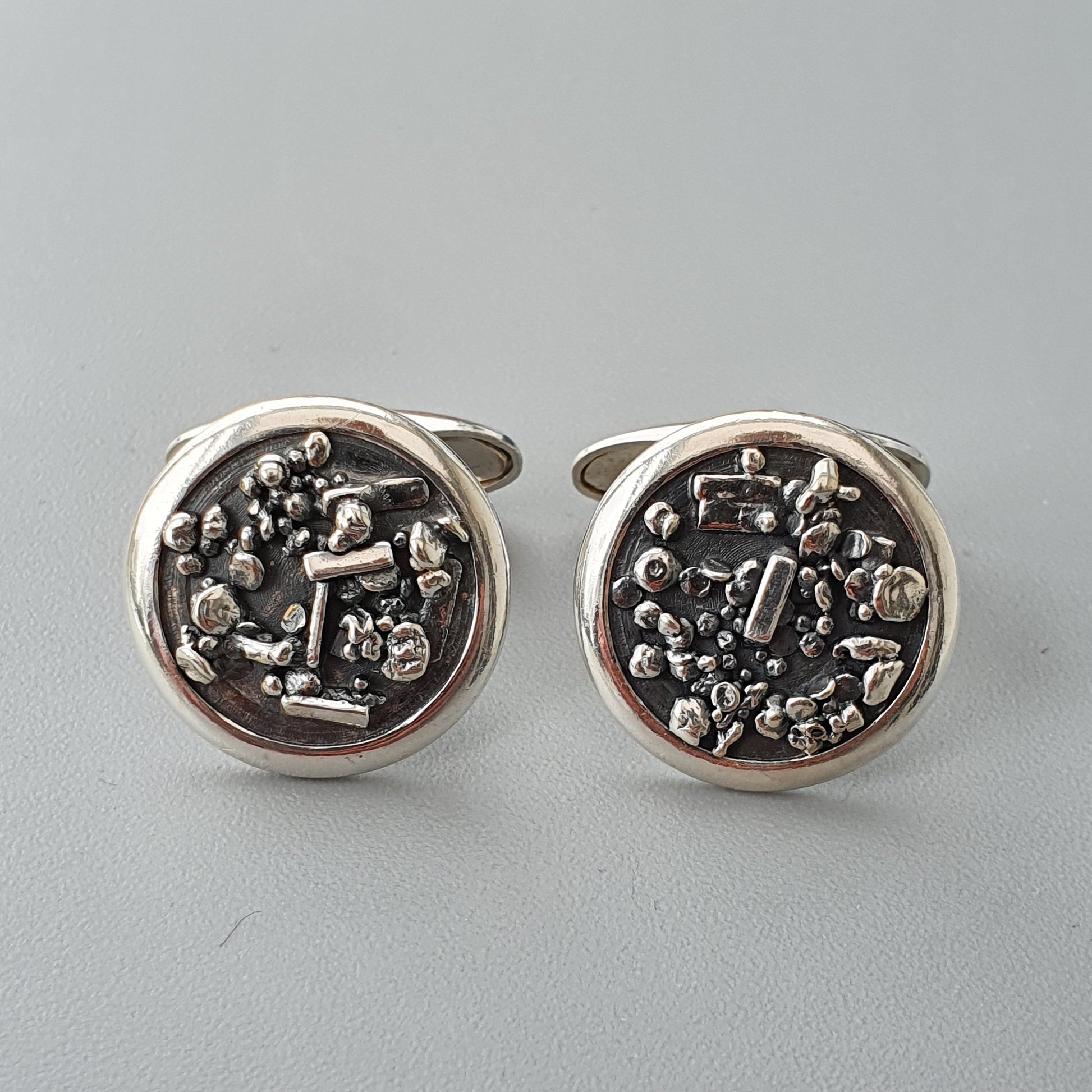 Pair of circular silver cufflinks with intricate metallic designs on their faces.