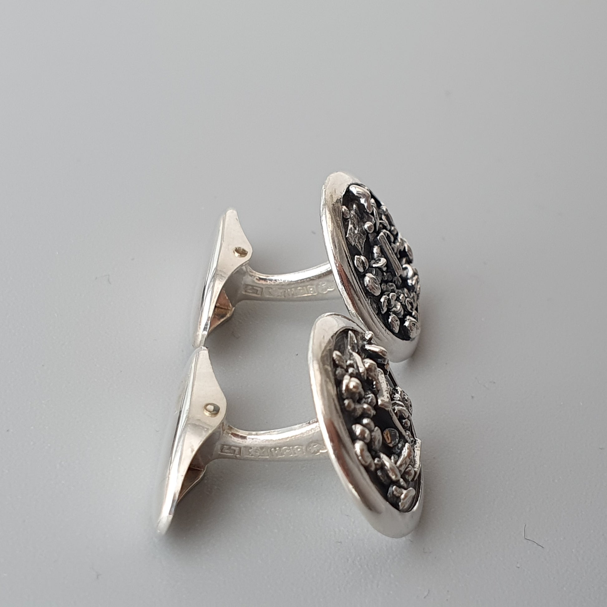 Pair of silver cufflinks with intricate floral or textured designs on oval faces.