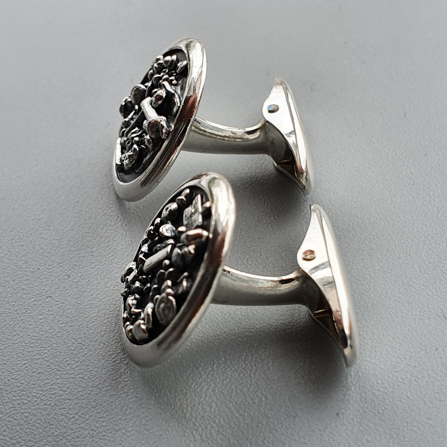 Pair of ornate silver cufflinks with intricate floral designs on oval faces.